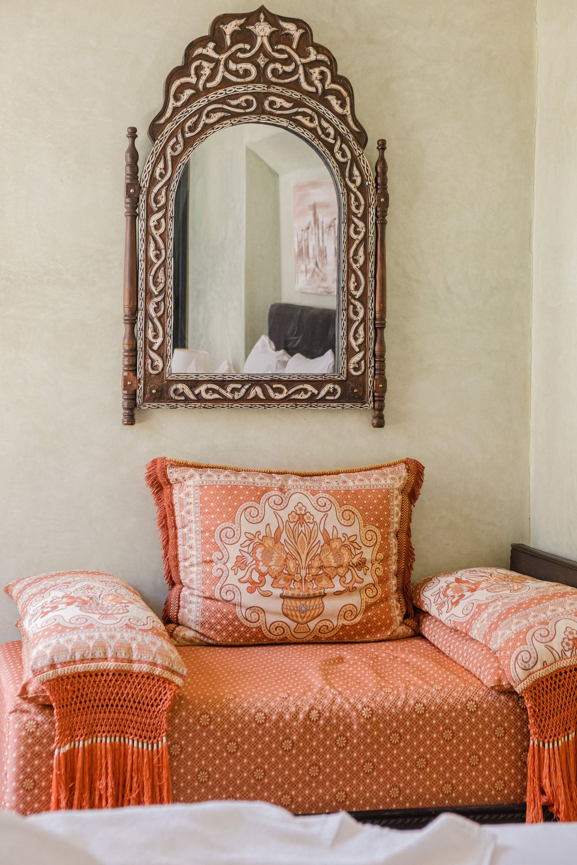 Ornate mirror above an orange patterned couch with fringed pillows.