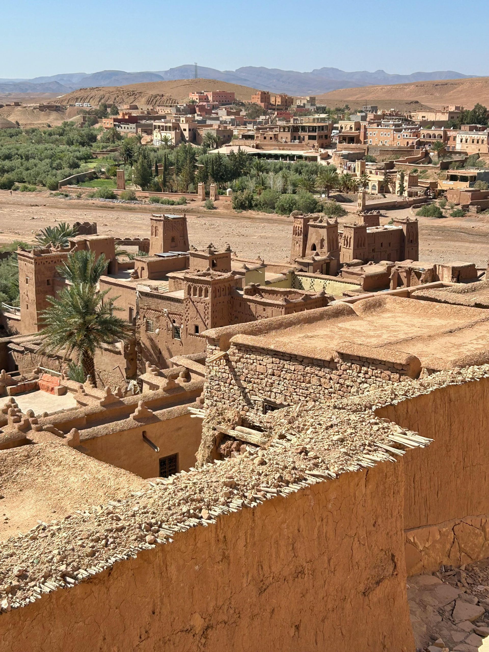 An ancient, brown mud-brick village nestled in a desert landscape, with a few palm trees.