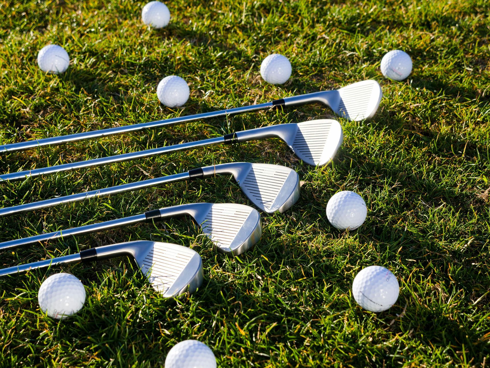 Five golf clubs lying on green grass among scattered white golf balls.