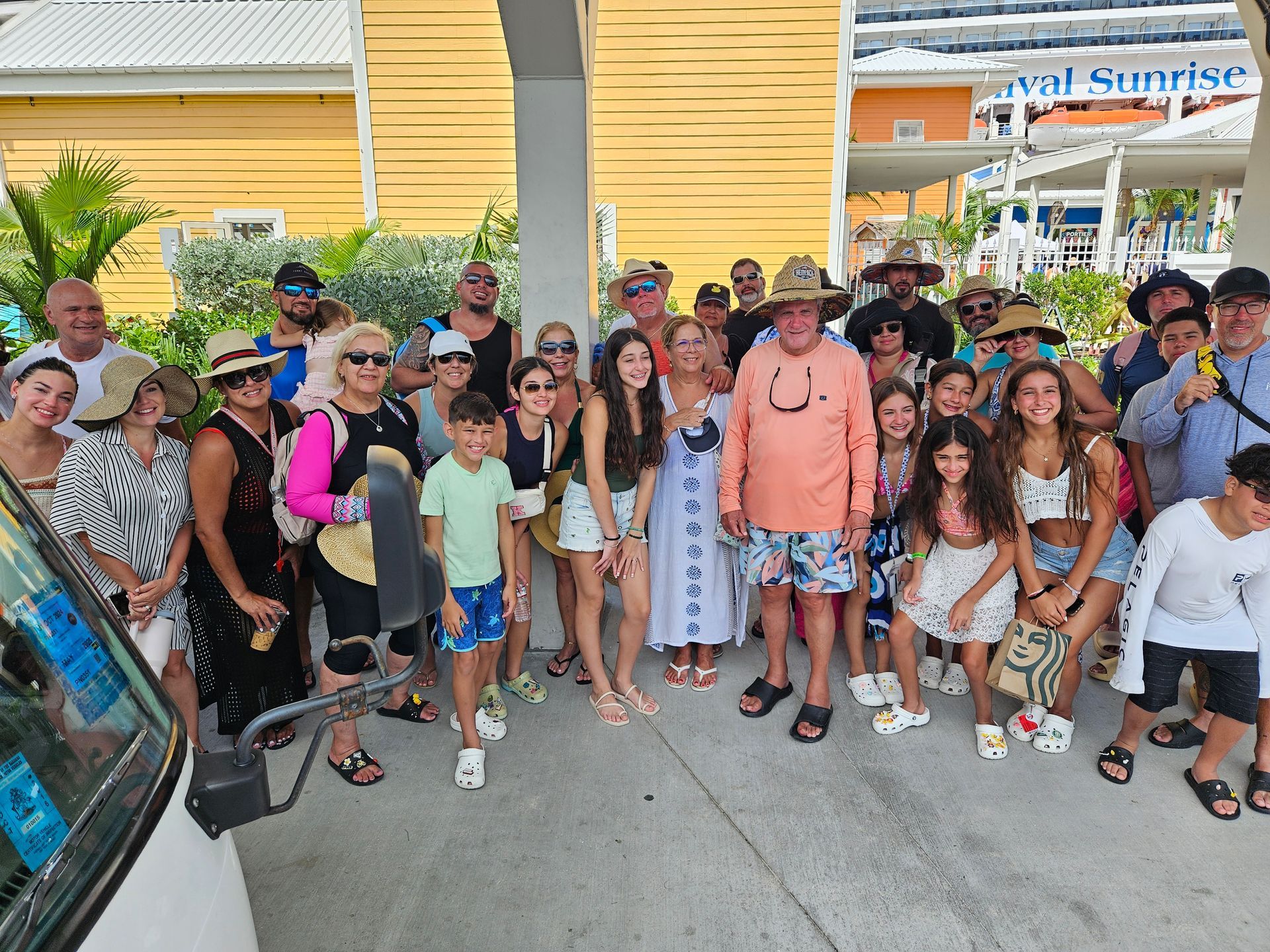 Group of people posing outdoors; sunny setting, yellow and orange buildings visible.