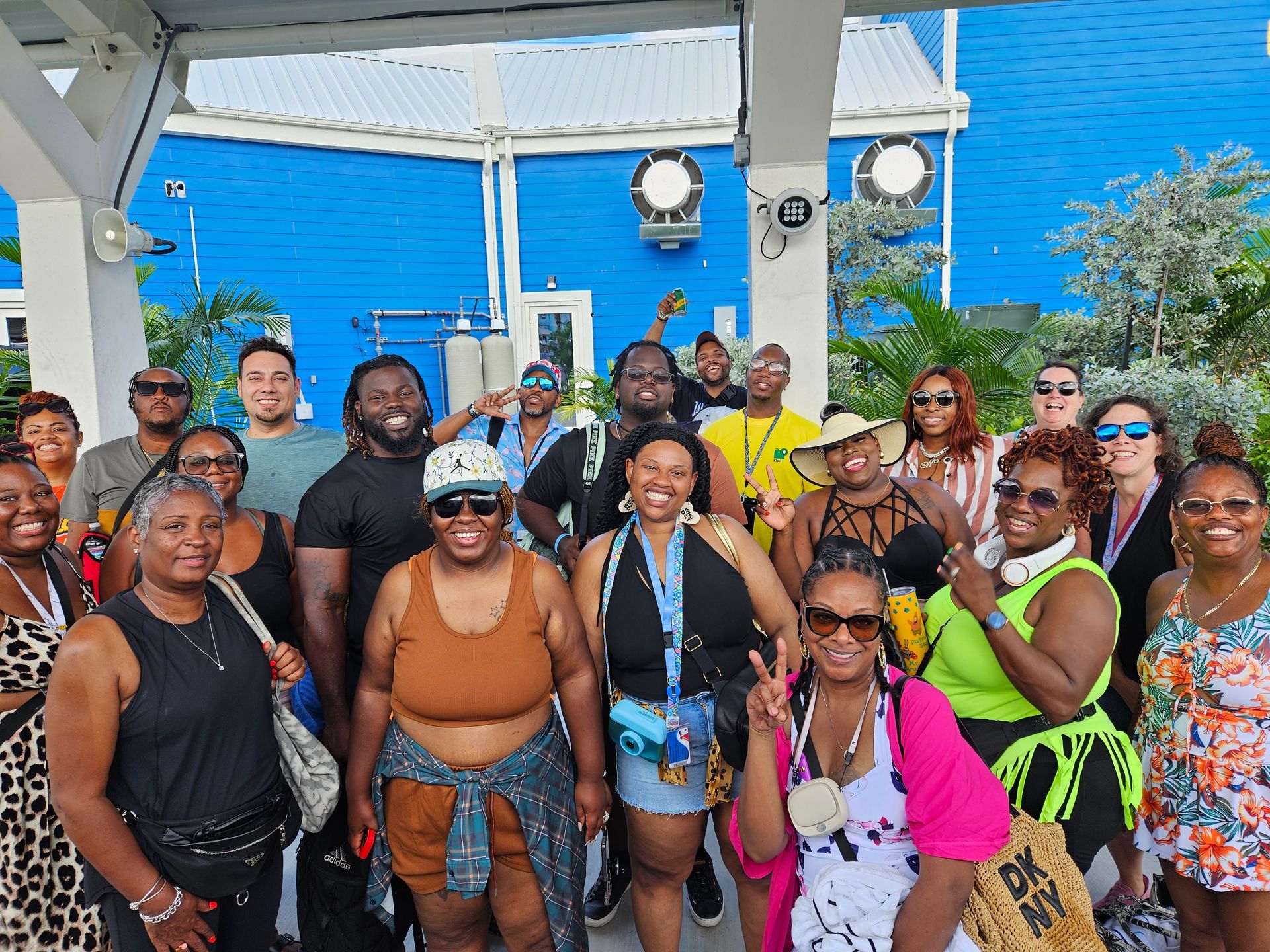 Group of people smiling, posing in front of blue building; sunny outdoor setting.