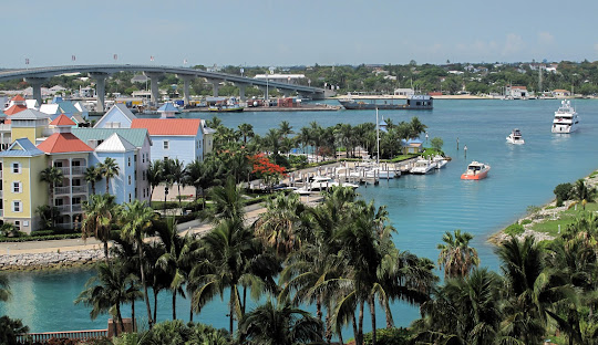 Harbor view with turquoise water, boats, palm trees, and colorful buildings under a blue sky.