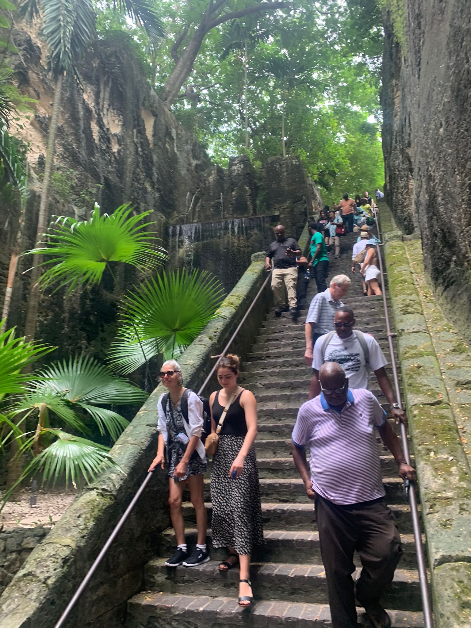 Stone staircase with tourists ascending; lush greenery surrounds, overcast sky.