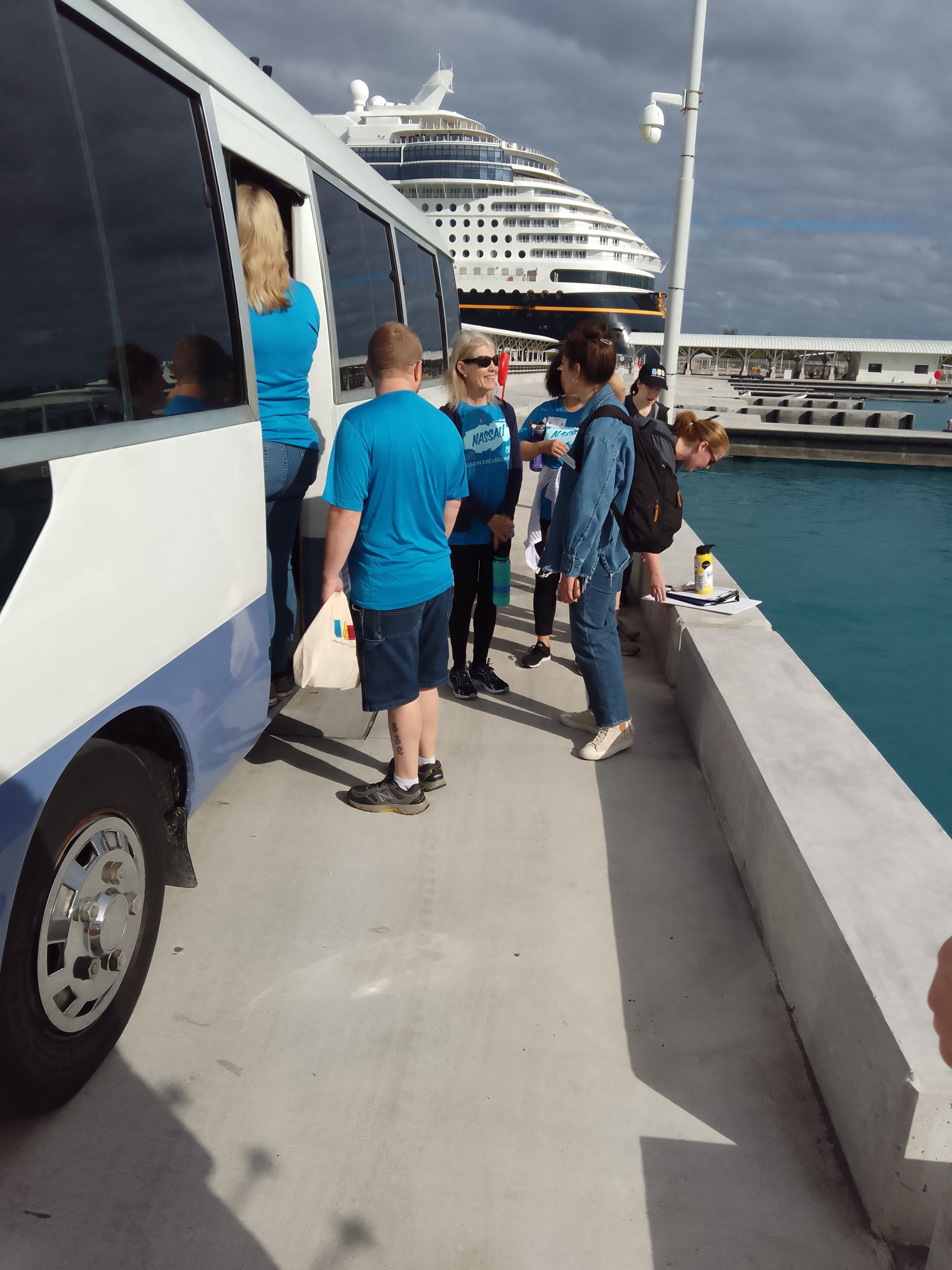 People getting off a bus near a cruise ship at a pier.