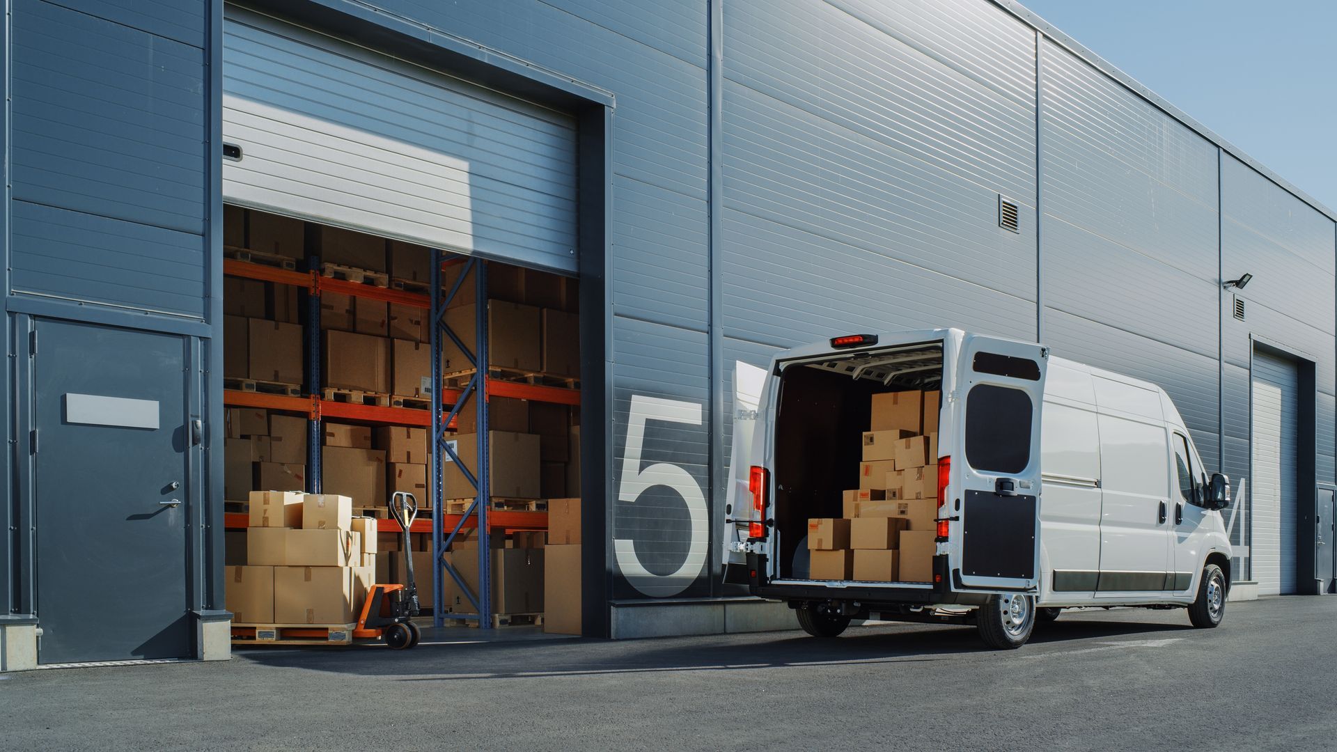 A white van is parked in front of a warehouse.