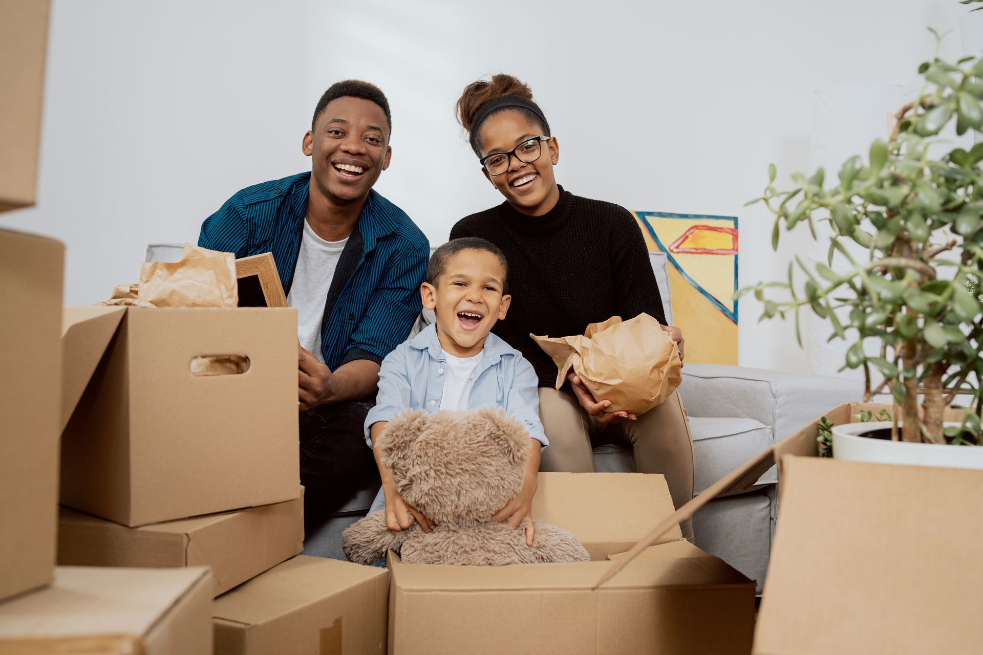 A family is sitting on a couch surrounded by cardboard boxes.