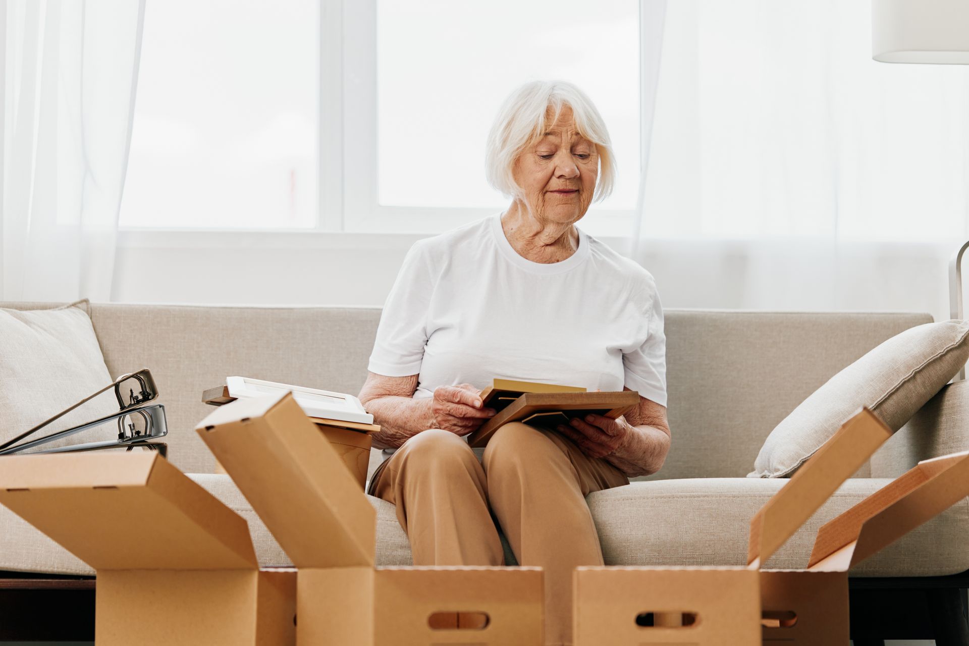 An elderly woman is sitting on a couch surrounded by cardboard boxes.