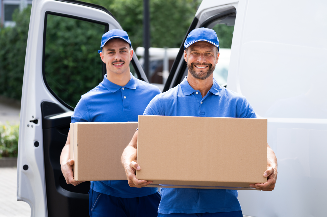 Two delivery men are carrying boxes out of a van.