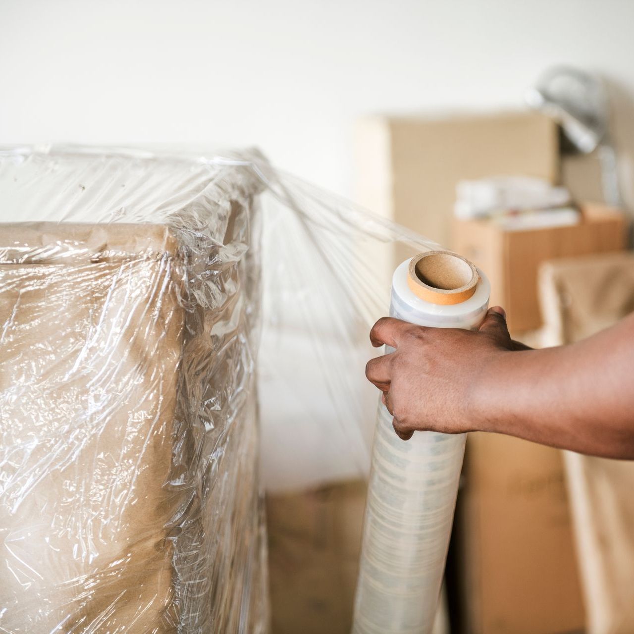 A person is wrapping a box with plastic wrap.