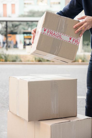 A person is putting a cardboard box on top of a stack of cardboard boxes.