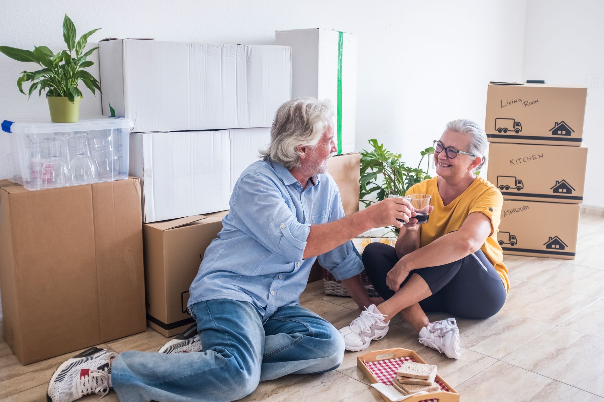 An elderly couple is sitting on the floor drinking wine.