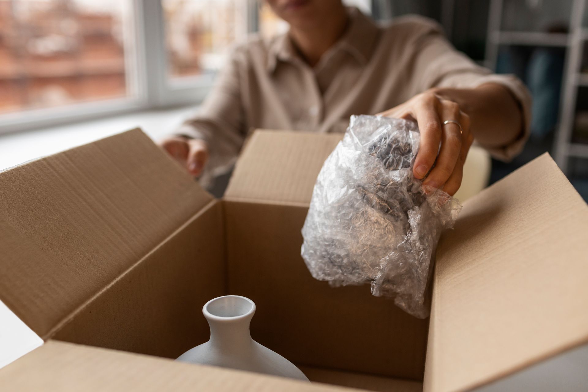 A woman is putting a vase in a cardboard box.