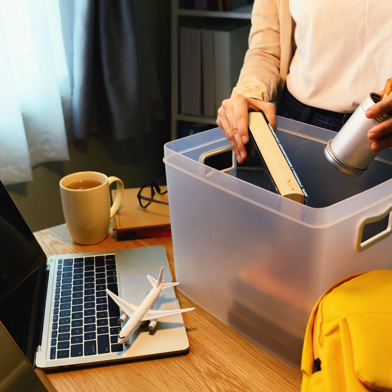 A woman is standing in front of a desk with a laptop and a plastic bin.