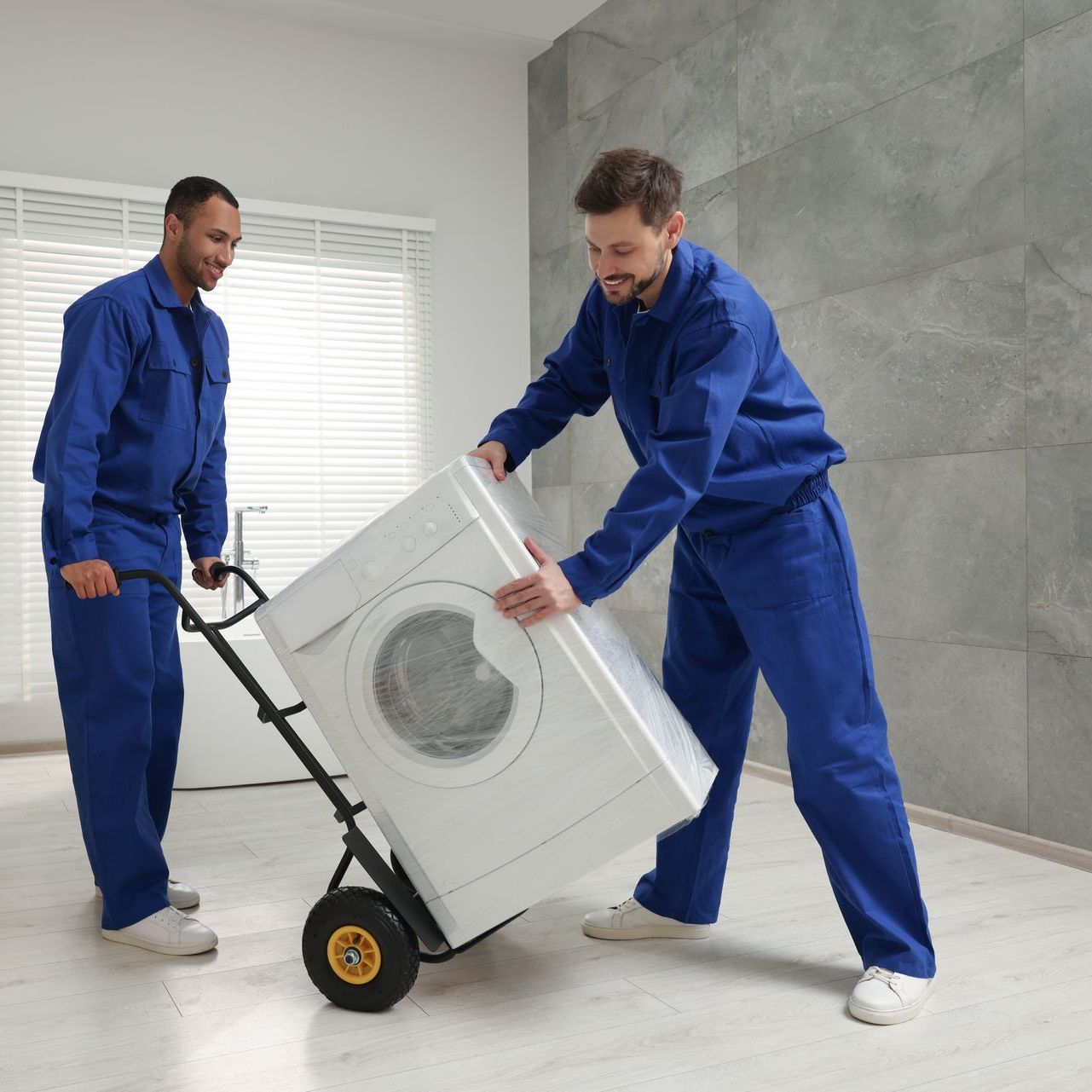 Two men are carrying a washing machine on a cart.