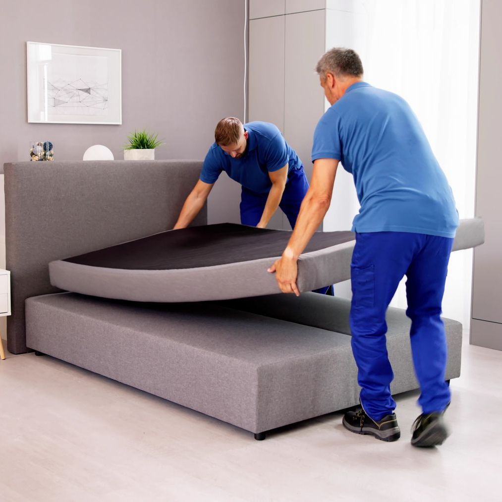 Two men are working on a bed in a bedroom.