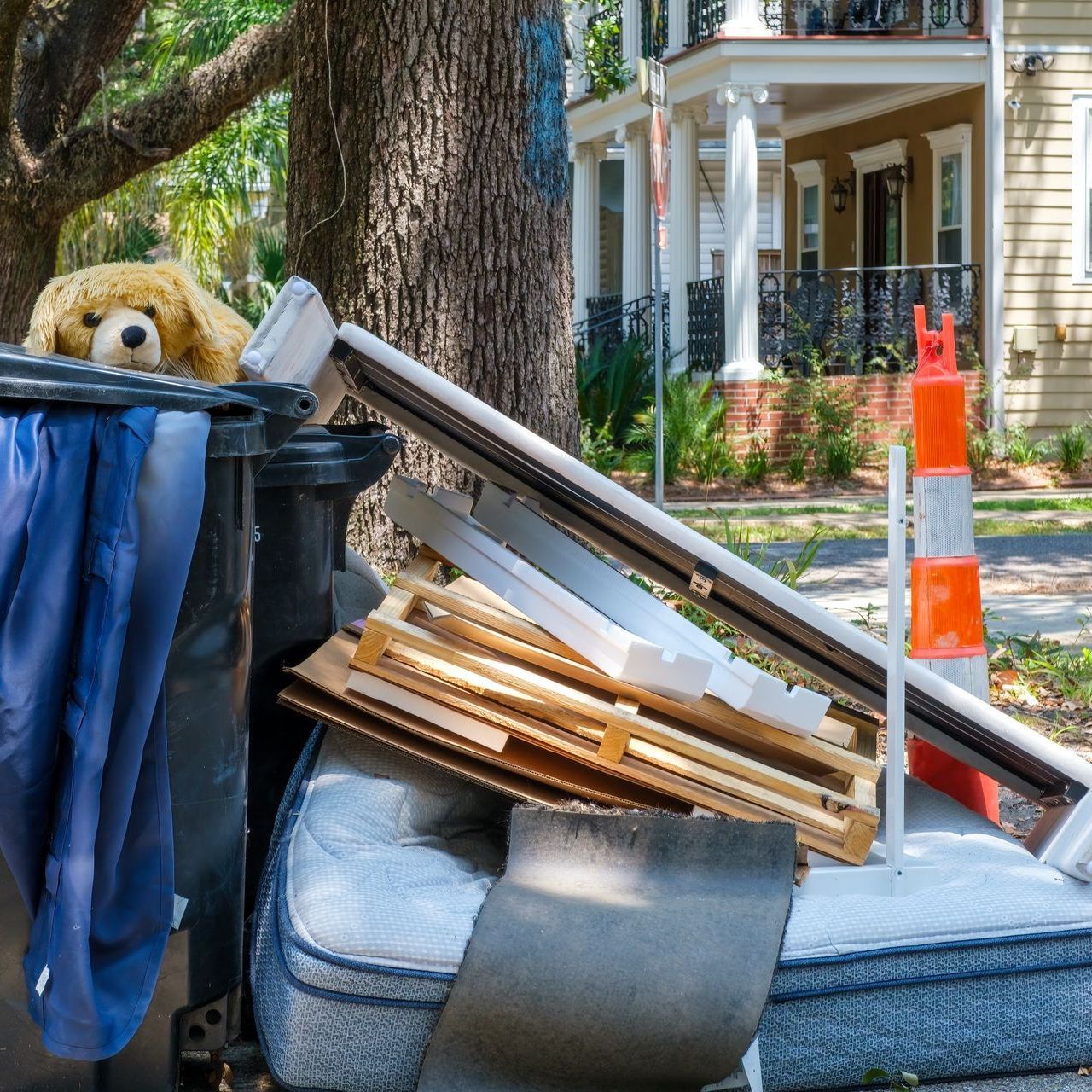 A teddy bear is sitting in a trash can next to a pile of trash.