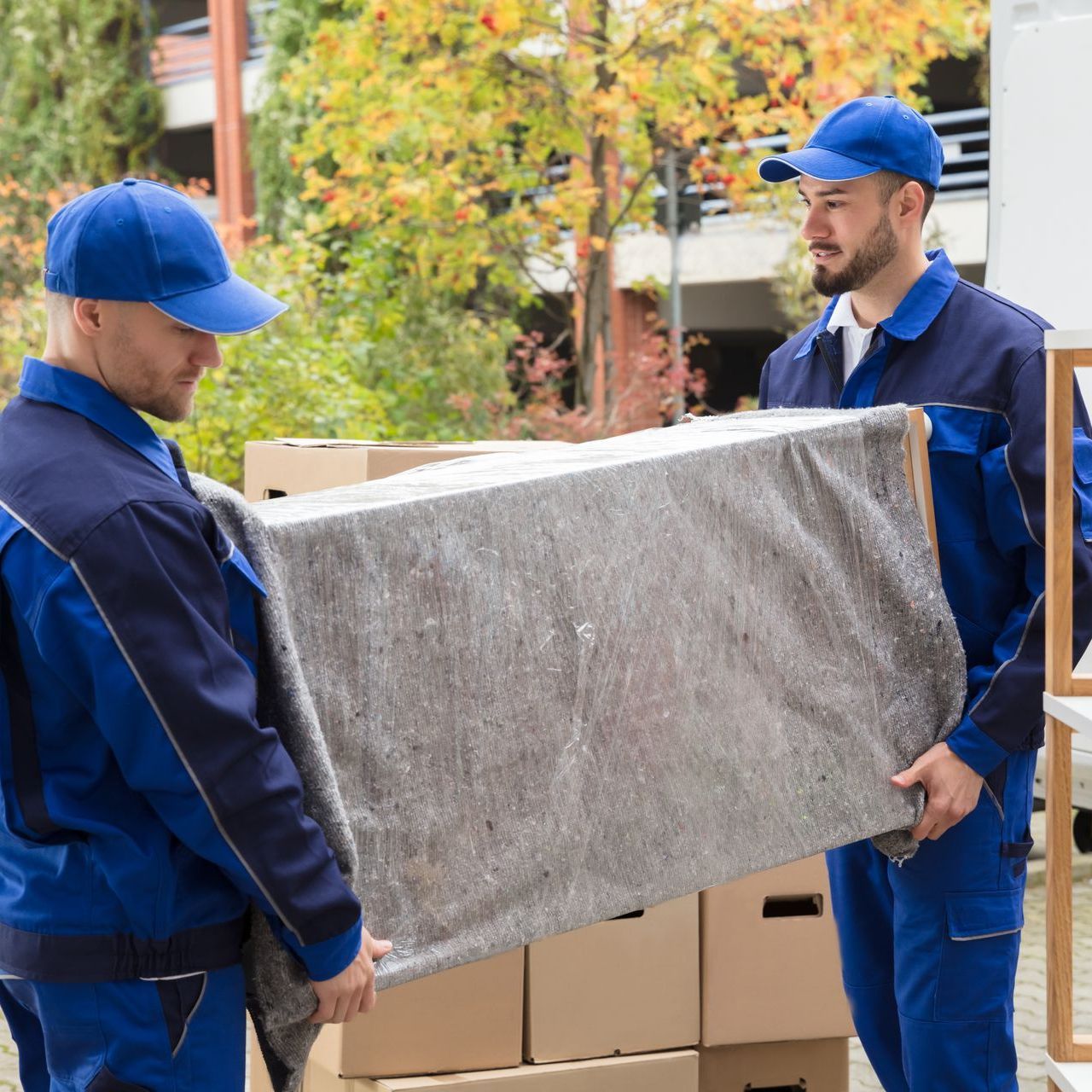 Two movers are carrying a couch in front of a van.