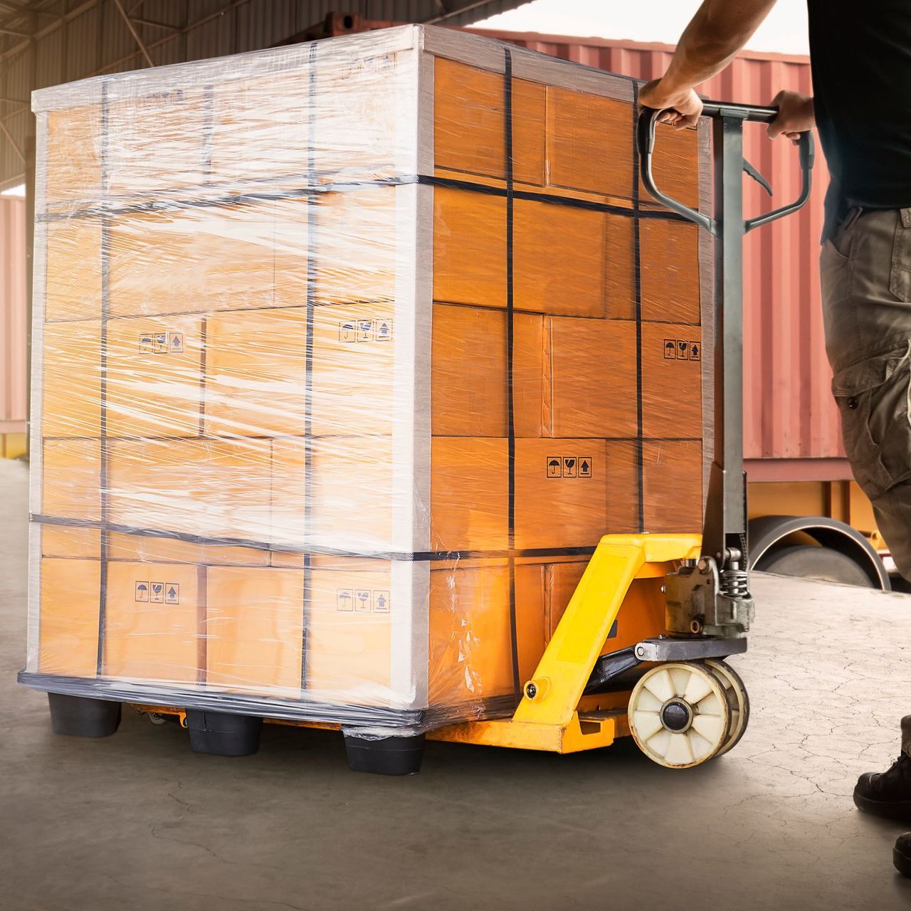 A man is pushing a pallet truck with boxes on it in a warehouse.