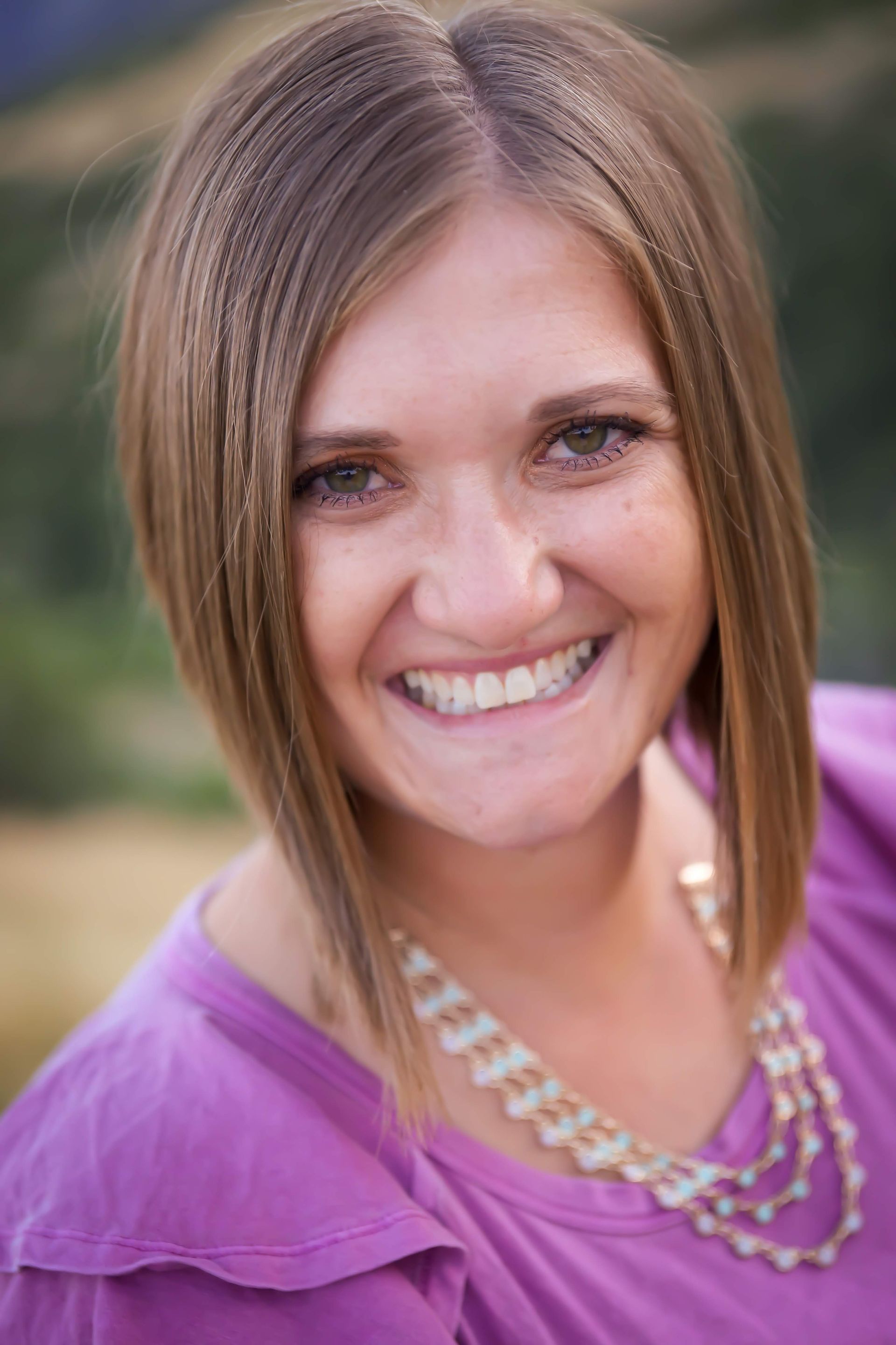 A woman wearing a purple shirt and a necklace is smiling for the camera.
