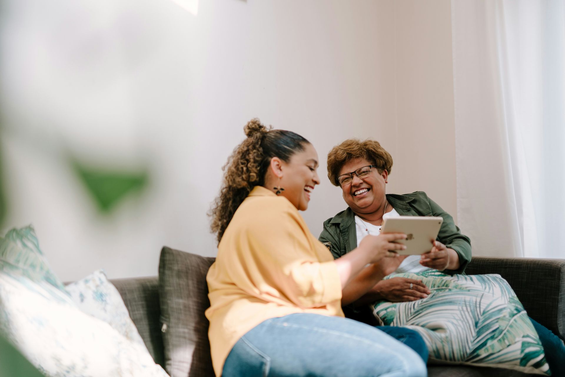 Two women are sitting on a couch looking at a tablet.