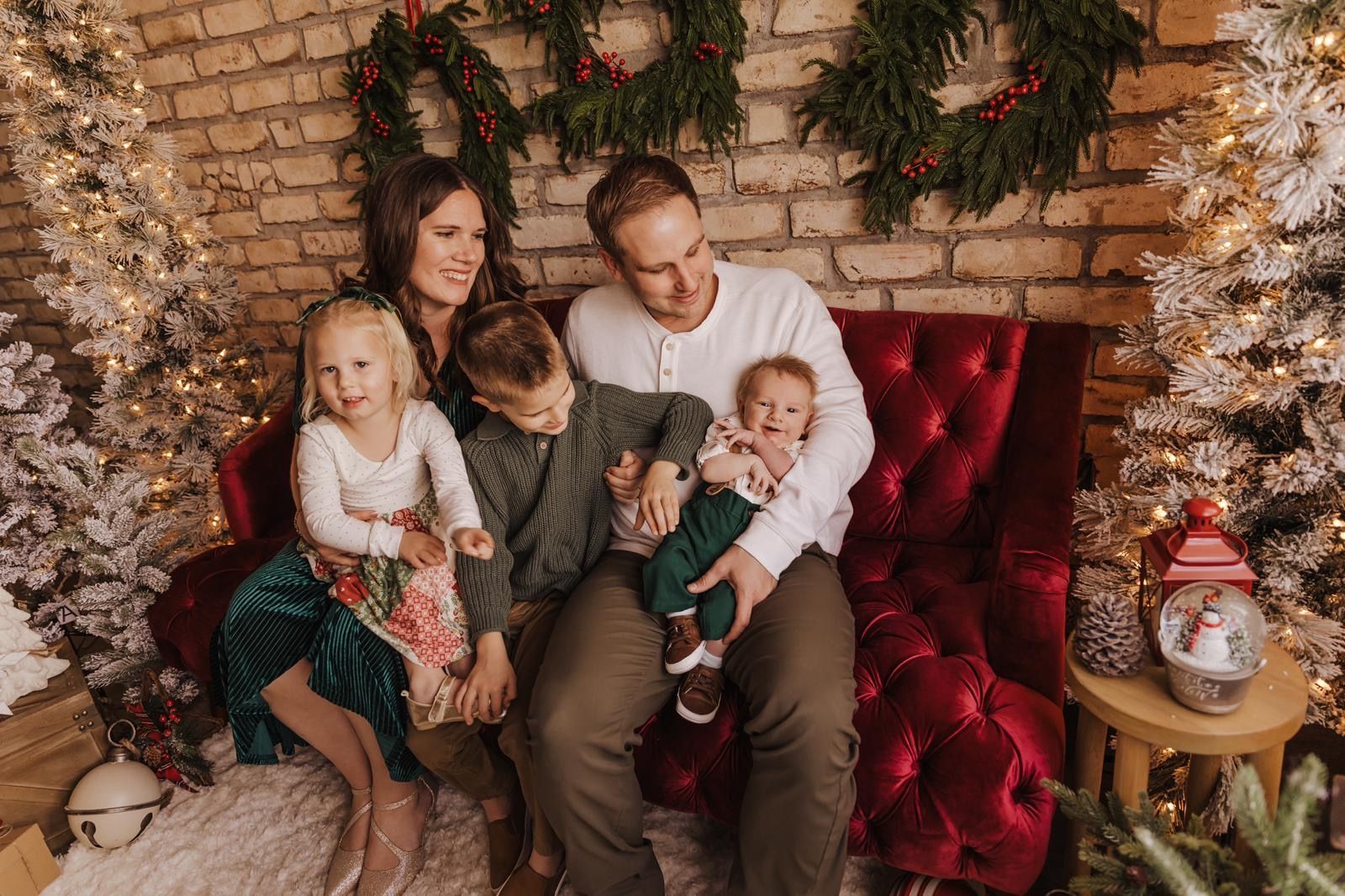 A family is sitting on a red couch in front of a christmas tree.