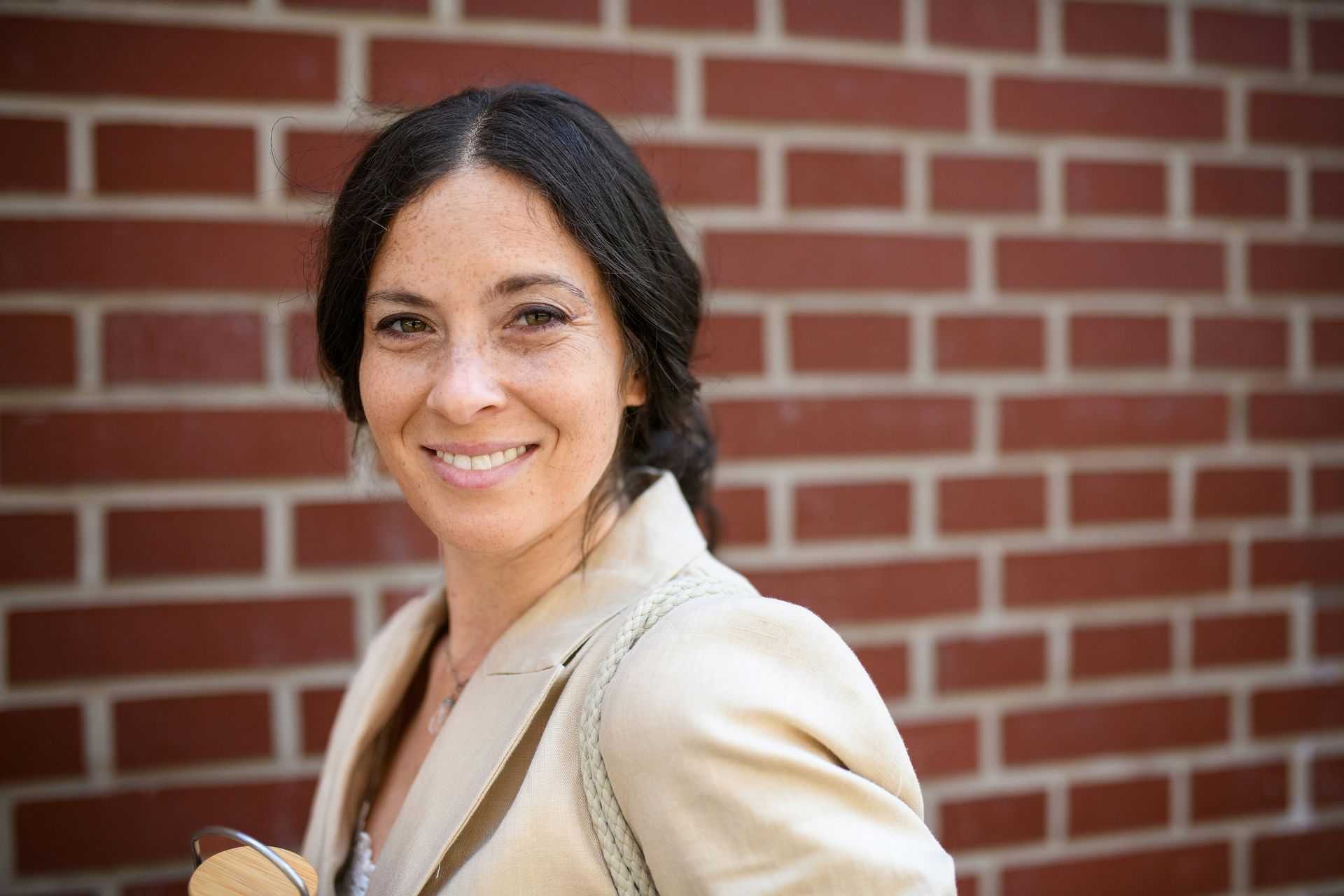 A woman is smiling in front of a brick wall.