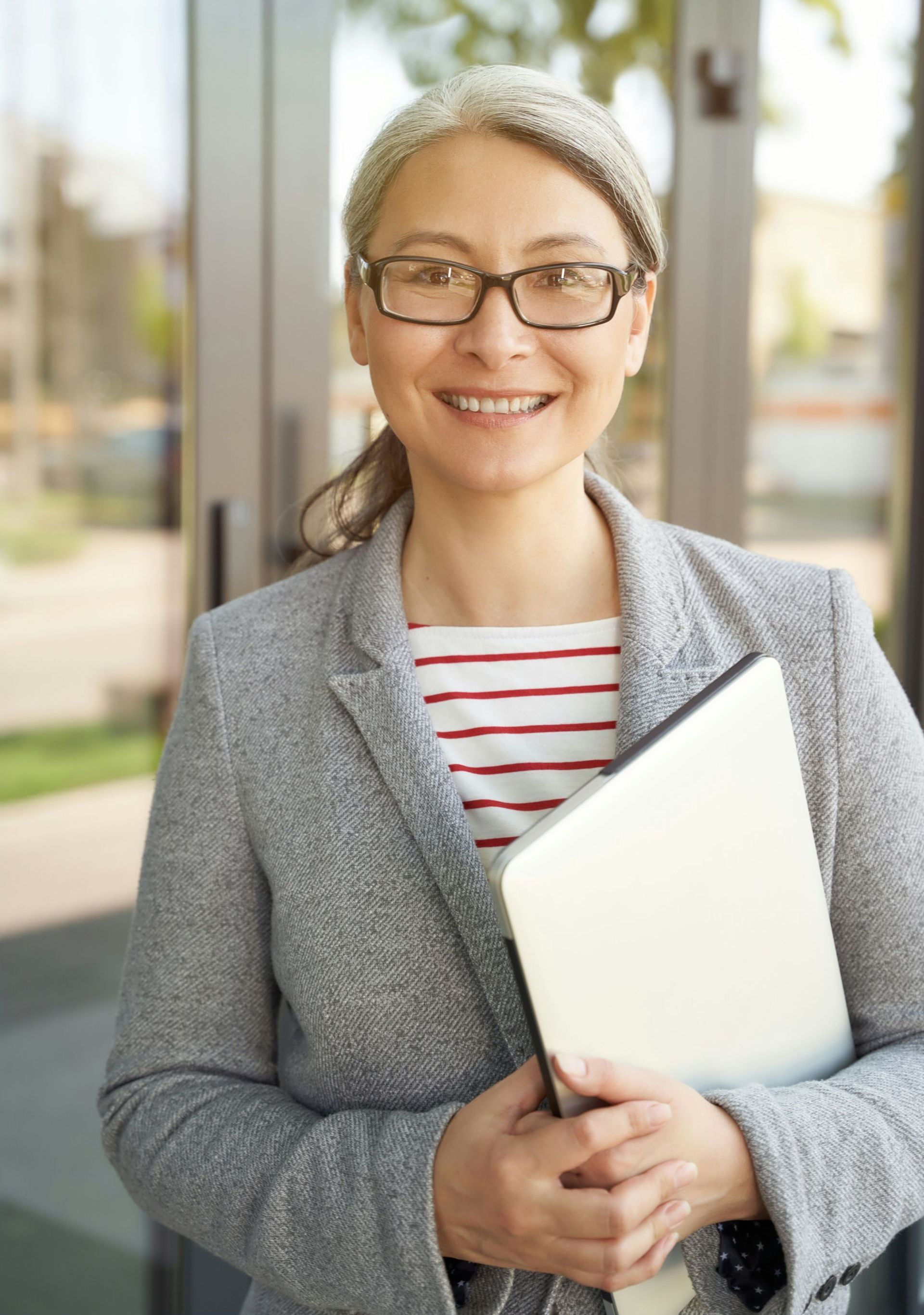 A woman wearing glasses and a hat is holding a book and a laptop.