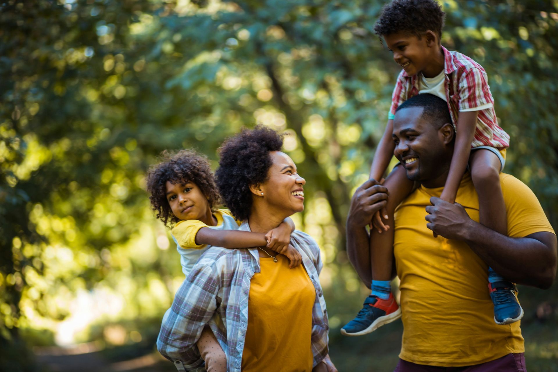 A man is carrying a child on his shoulders in a park.