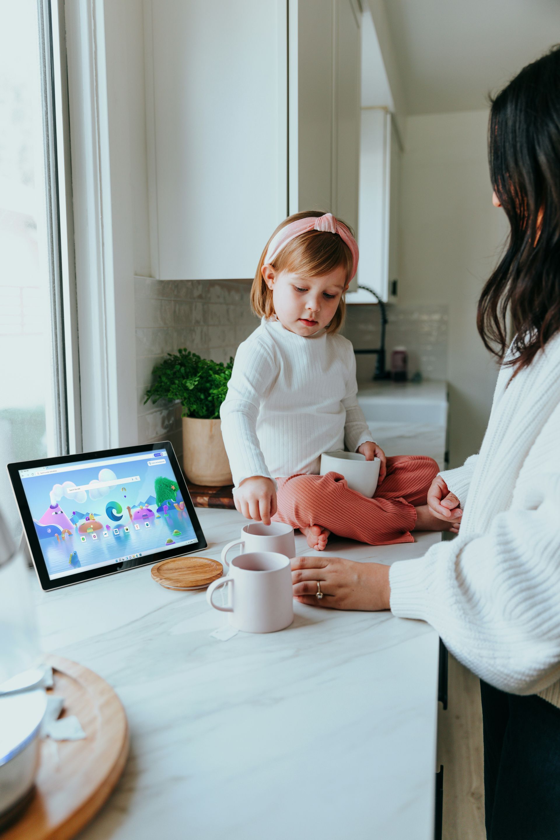 A woman is standing next to a little girl sitting on a counter.