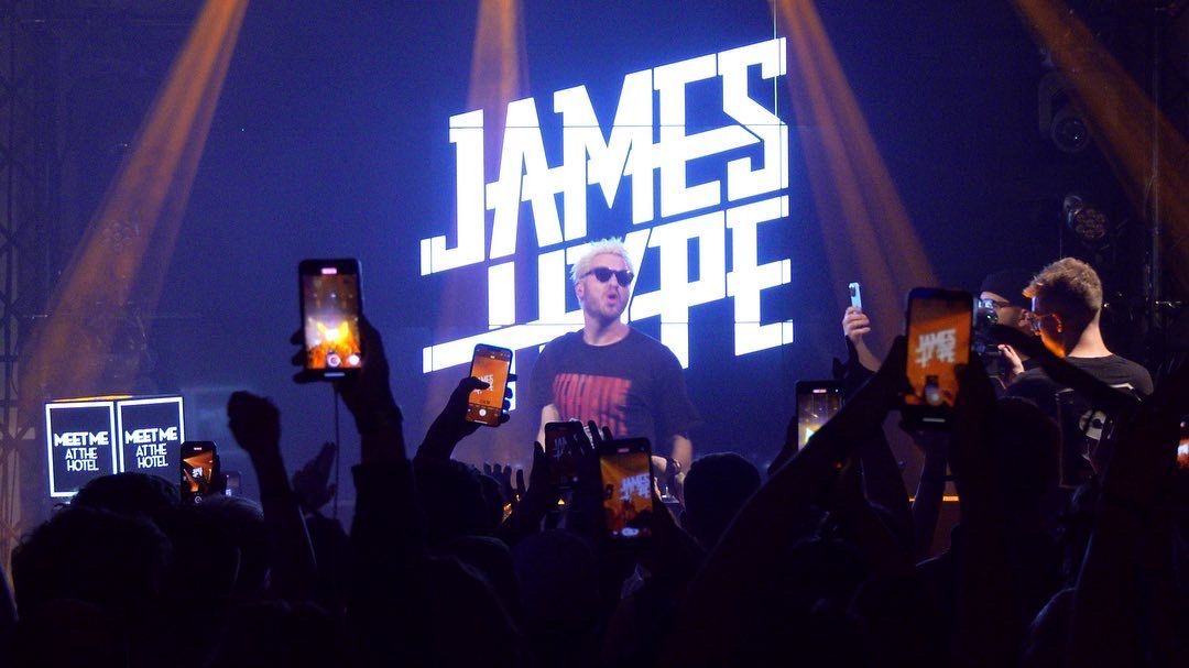 James Hype treedt op het podium op onder zijn eigen naam in felwitte letters, terwijl het publiek zijn telefoon omhoog houdt.