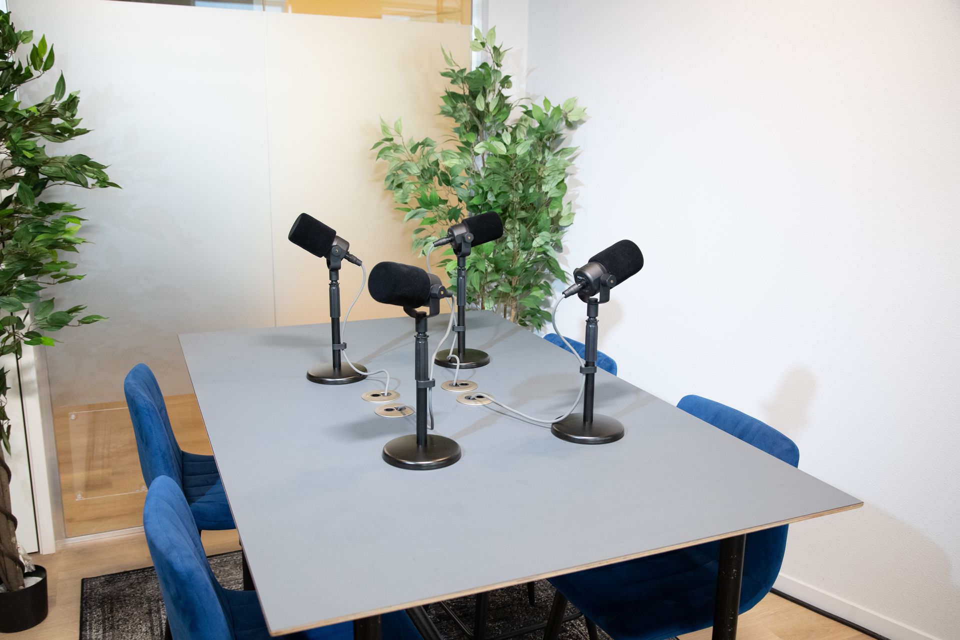 Podcaststudio met microfoons op een grijze tafel, blauwe stoelen en groen.