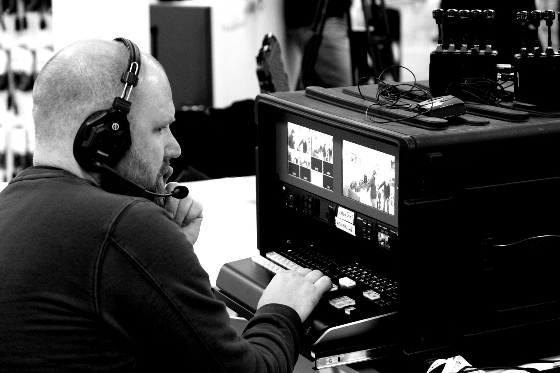 Man met headset bedient videobewerkingsapparatuur en concentreert zich op meerdere schermen.