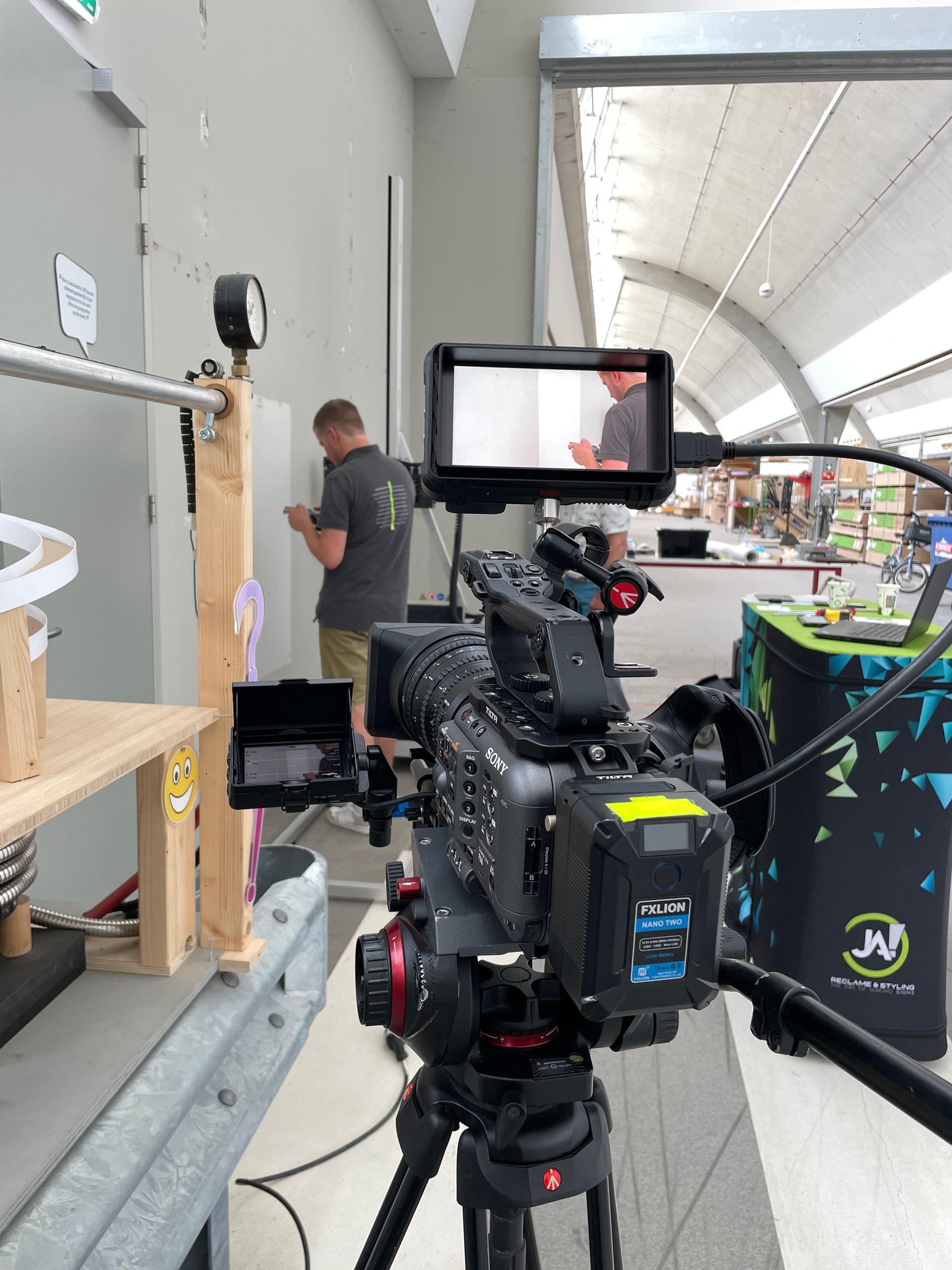 Een videocamera filmt een man die aan een muur werkt. 