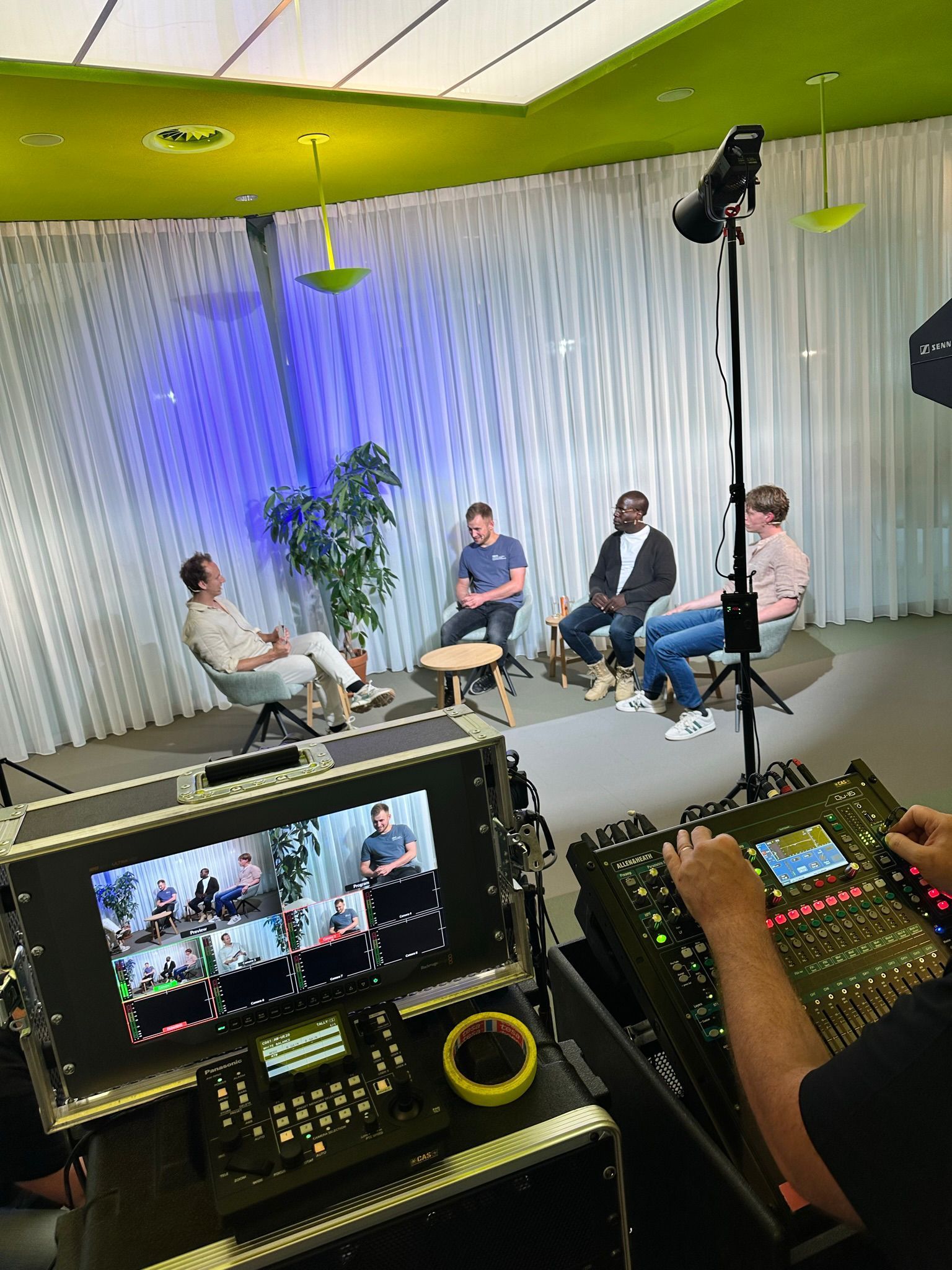 Vier mensen op de set van een talkshow, met een blauw/witte achtergrond.