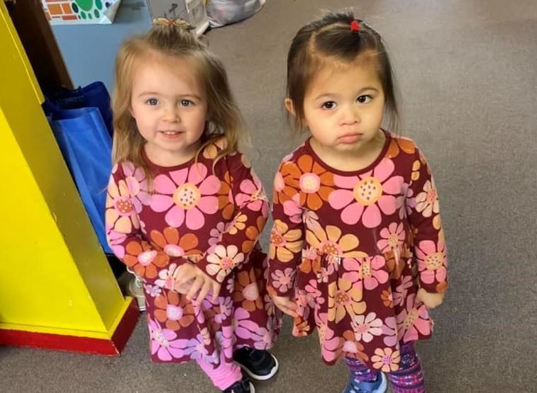 Two little girls wearing floral dresses are standing next to each other