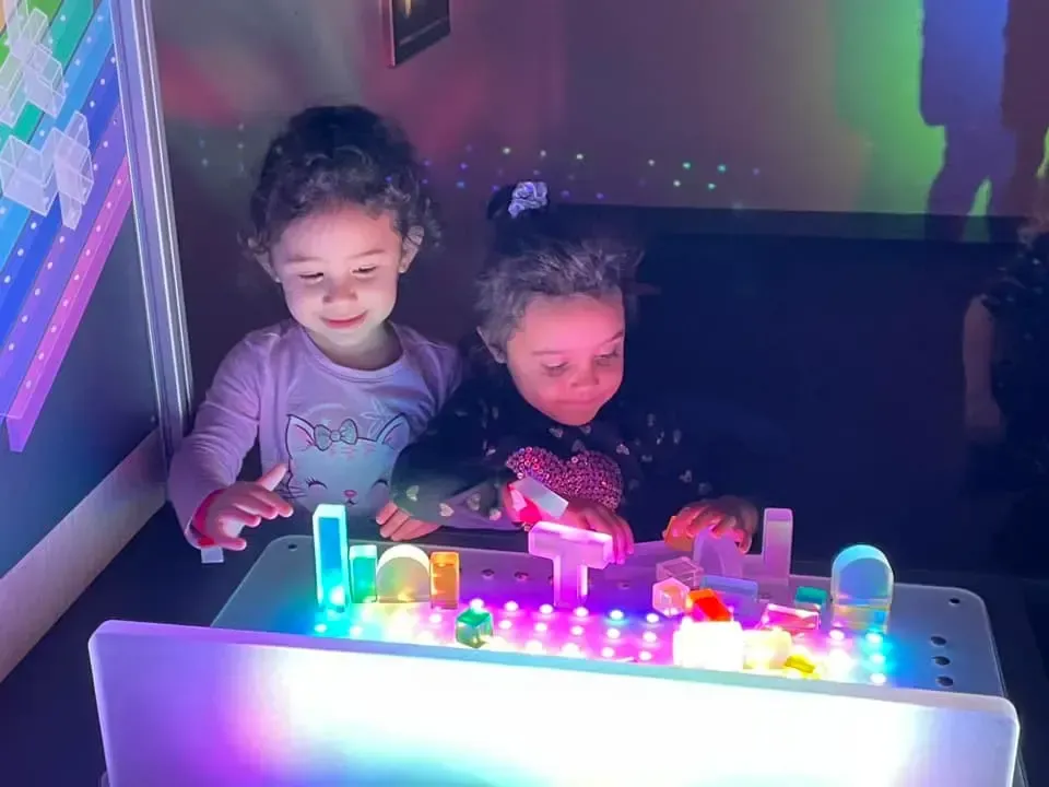 Two little girls are playing with a light table.