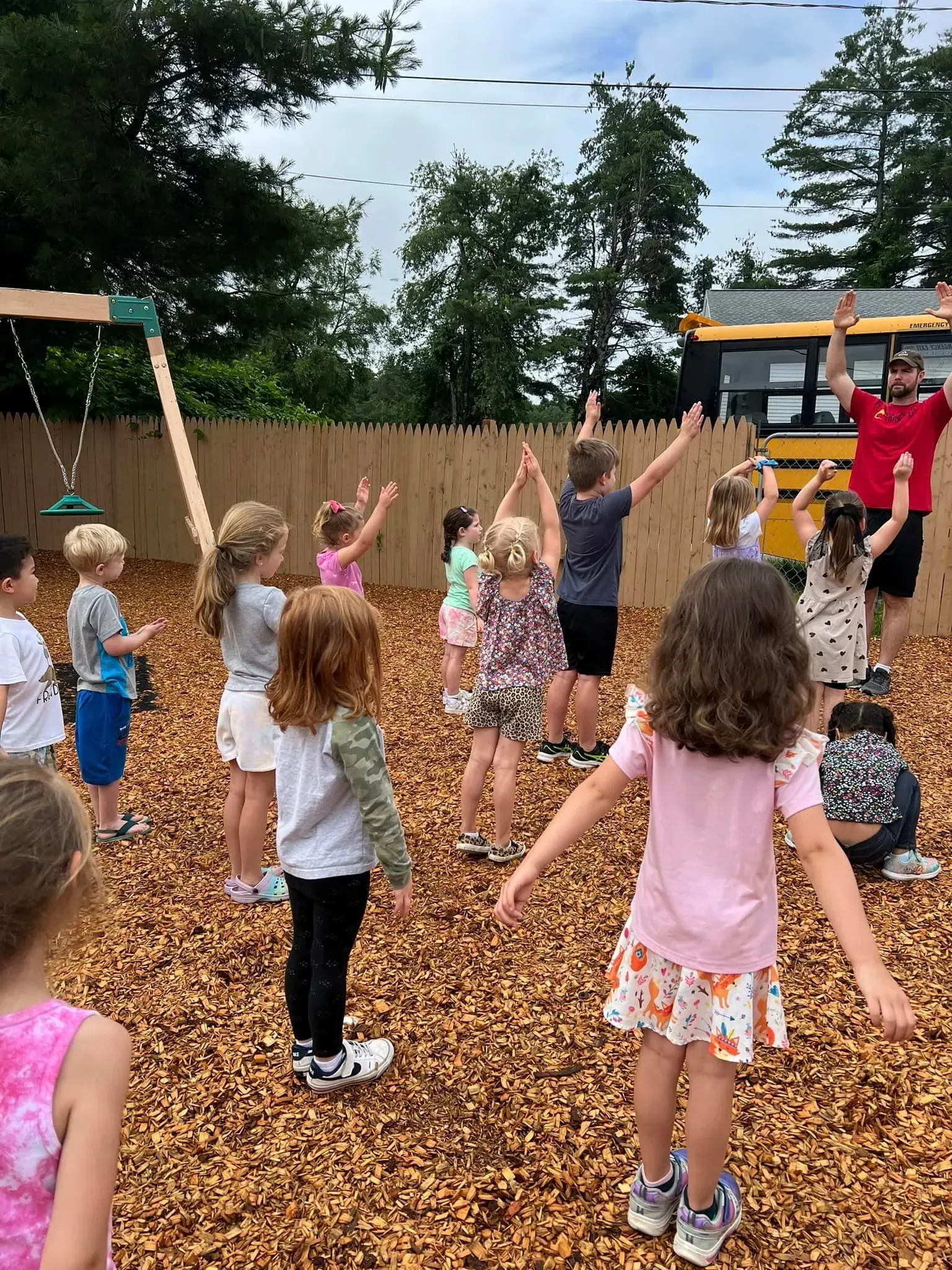 A group of children are standing in a playground with their arms in the air.