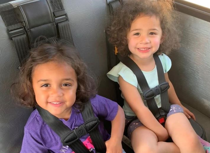 Two little girls are sitting in car seats and smiling for the camera.