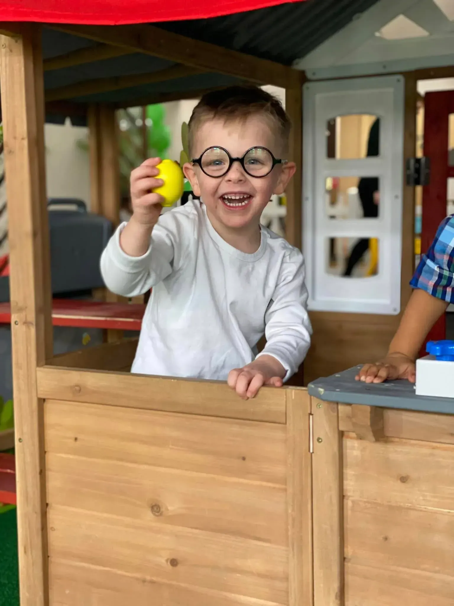 A little boy wearing glasses is holding a yellow ball in a playhouse.