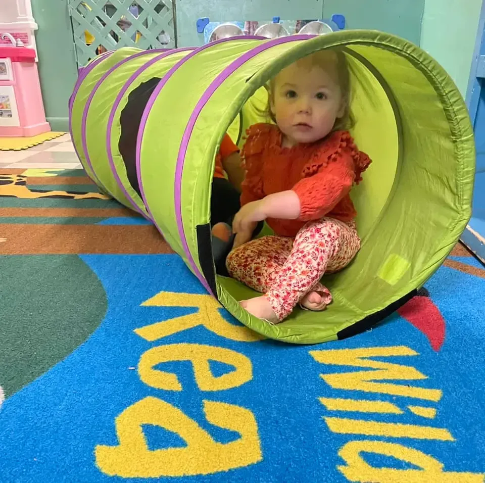 A little girl is sitting in a green and purple tunnel