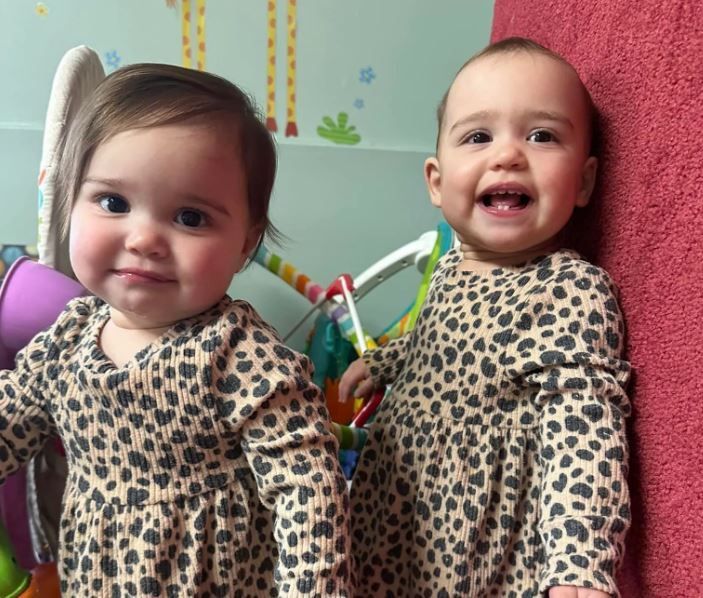 Two babies wearing leopard print dresses are standing next to each other