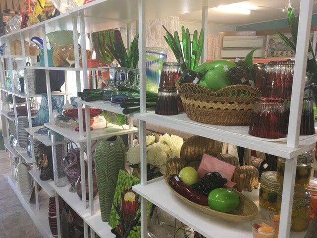 a shelf filled with vases , bowls , candles , and fruit .