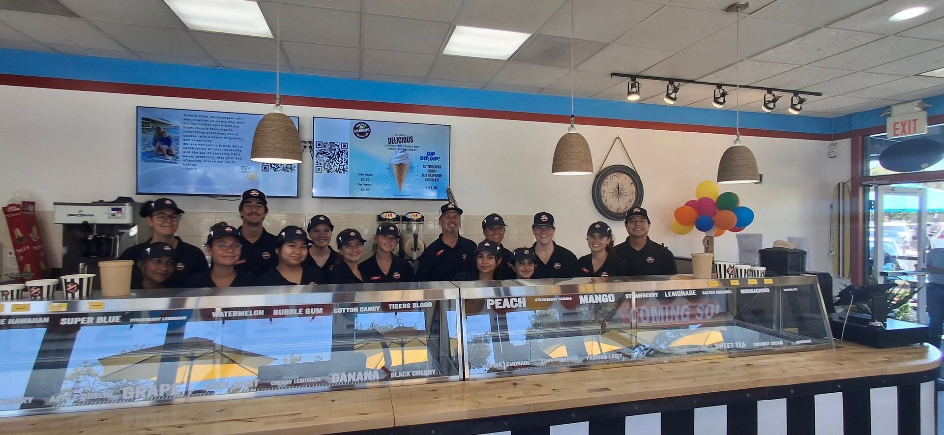 A group of staff members in matching uniforms stand behind an ice cream shop counter.