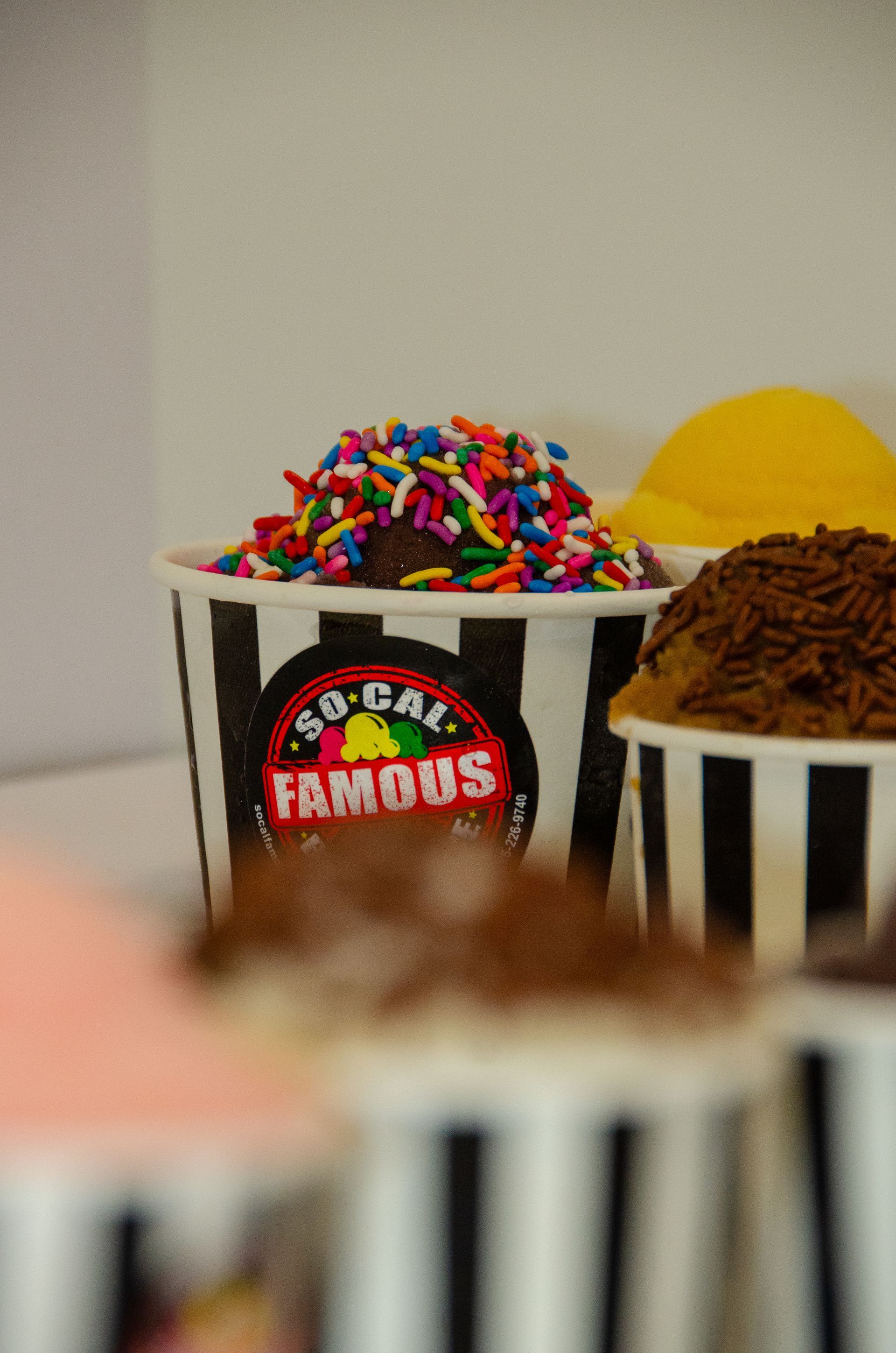 Several cups of frozen yogurt topped with sprinkles and chocolate shavings in black-and-white striped cups.