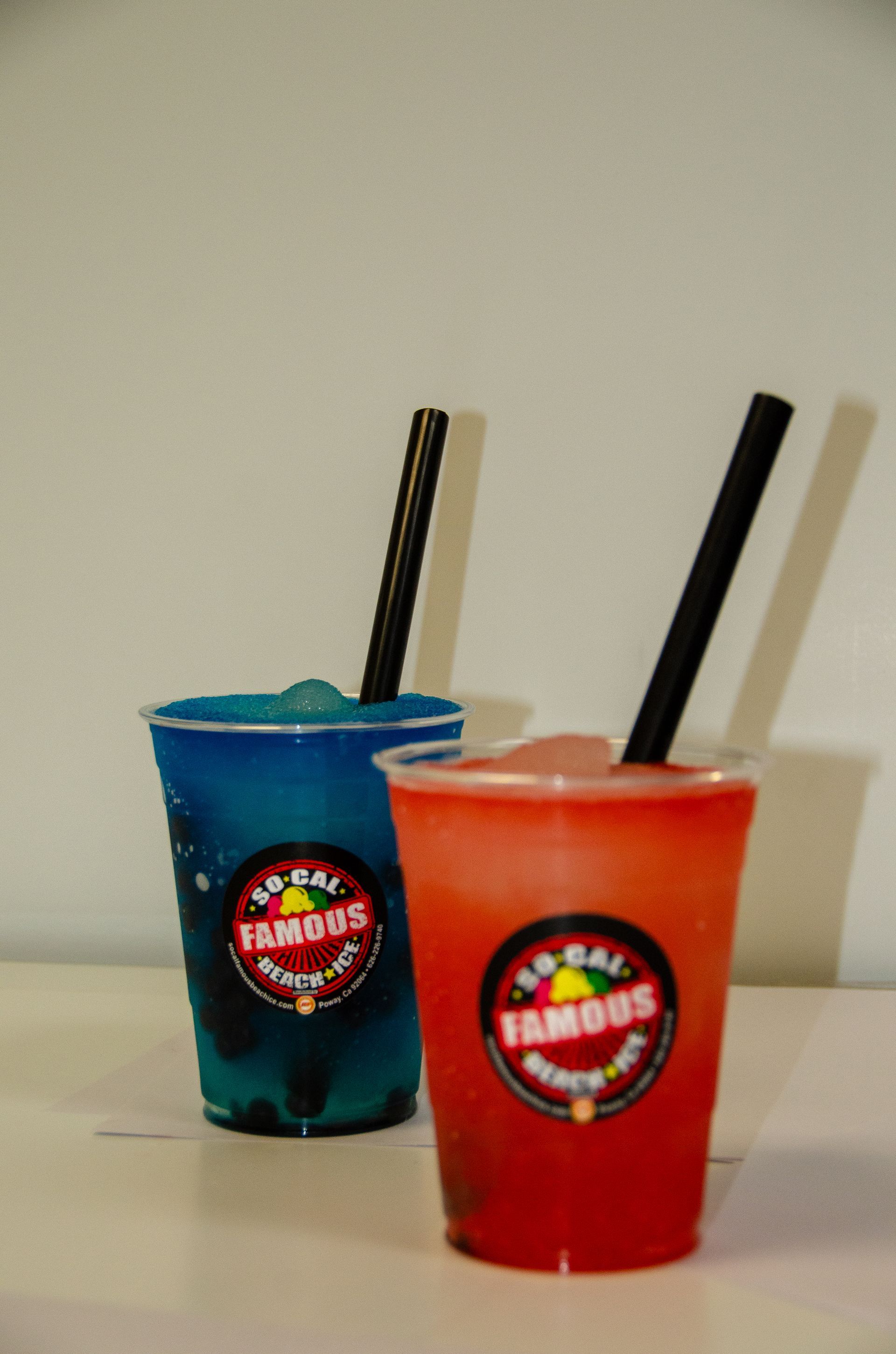 Two plastic cups of slushy drinks, one blue and one red, both with black straws and a 