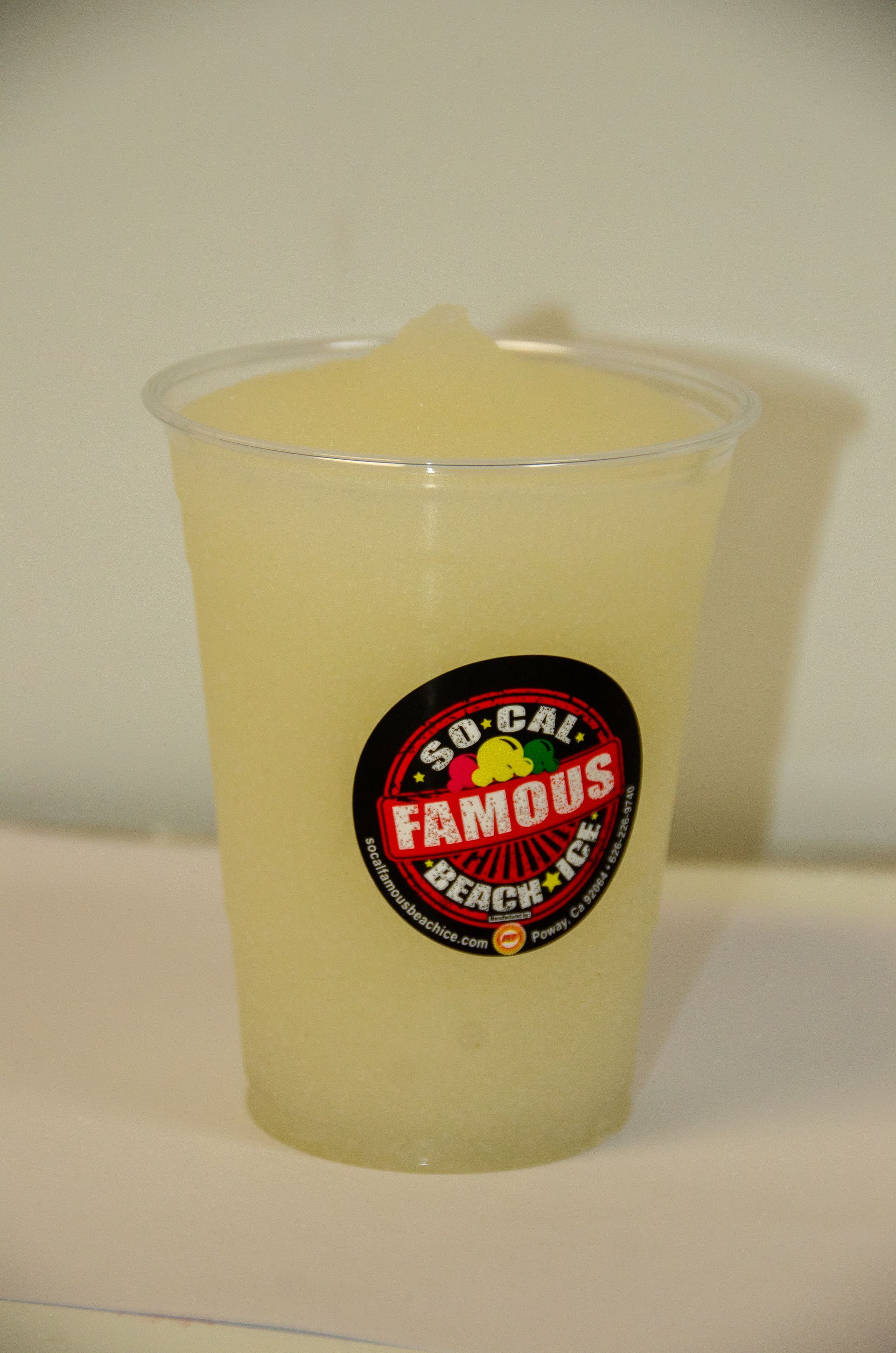 A clear plastic cup of slushy, light yellow shaved ice with a round 
