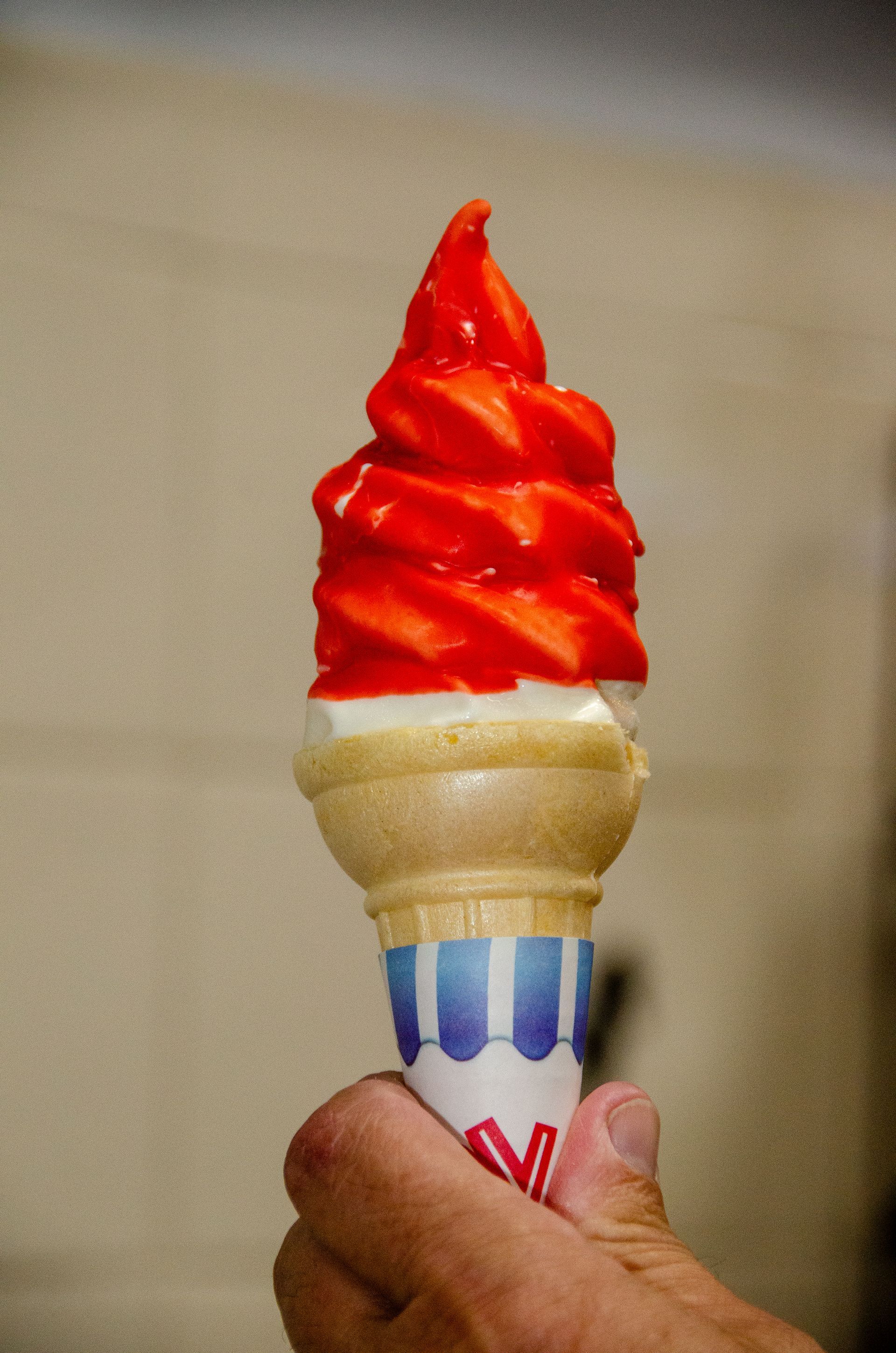 A hand holds a soft-serve ice cream cone dipped in a bright orange, hard-shell coating.