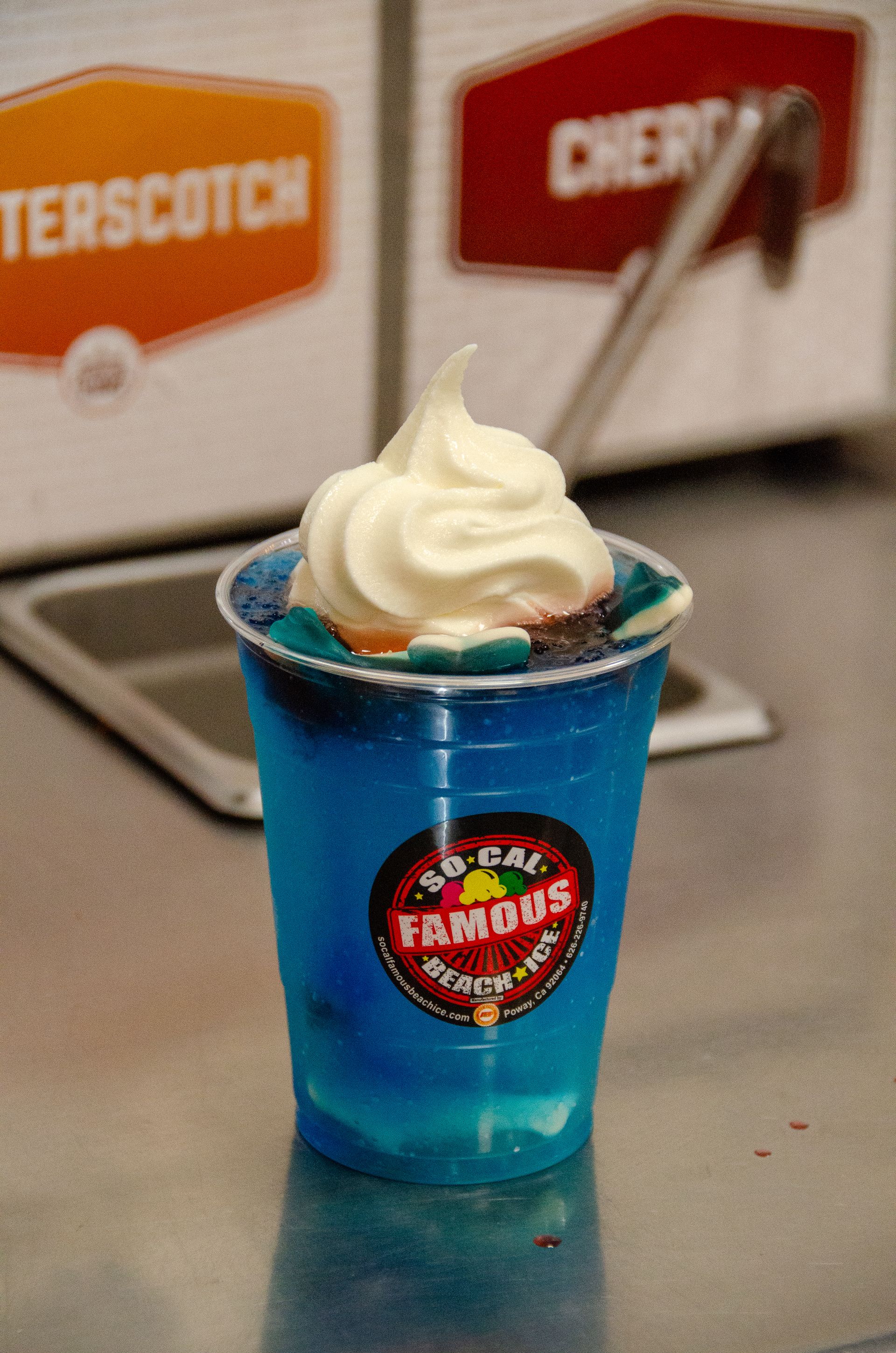 A blue slushy drink topped with soft-serve ice cream in a clear plastic cup with a 