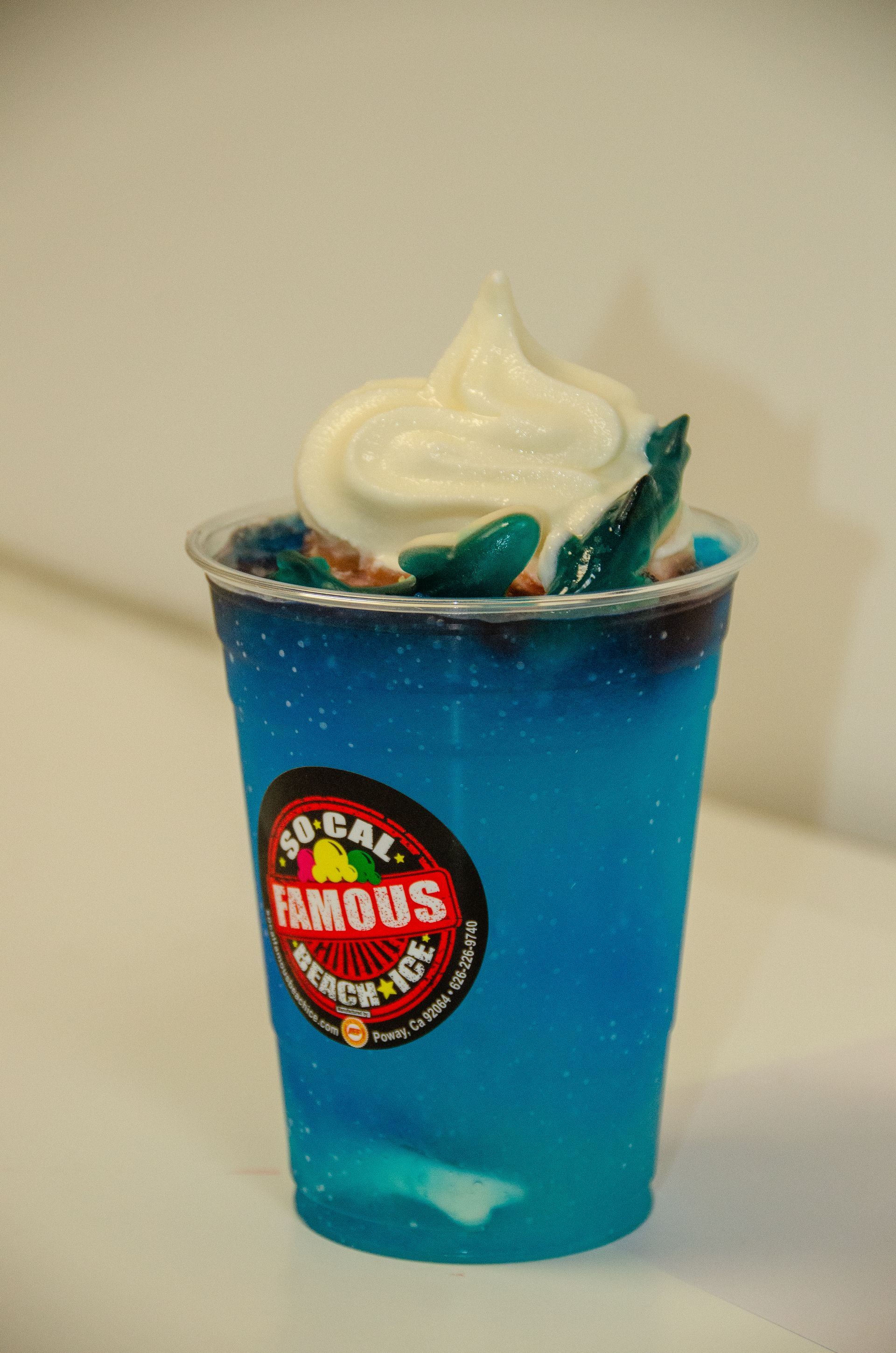A bright blue frozen drink in a clear plastic cup topped with a swirl of white soft-serve ice cream.