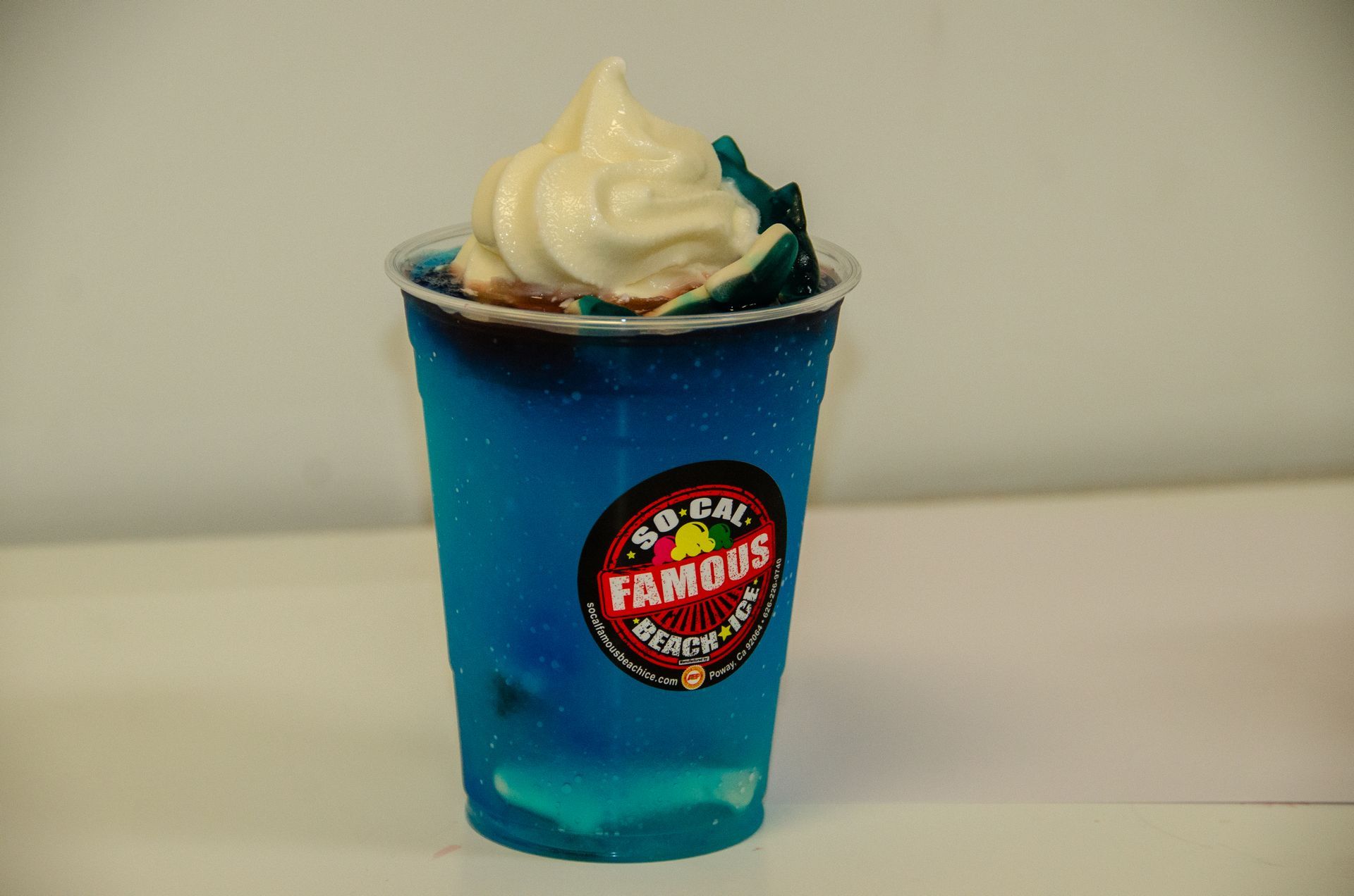 A blue slushie drink topped with a swirl of soft-serve ice cream, in a clear plastic cup with a 